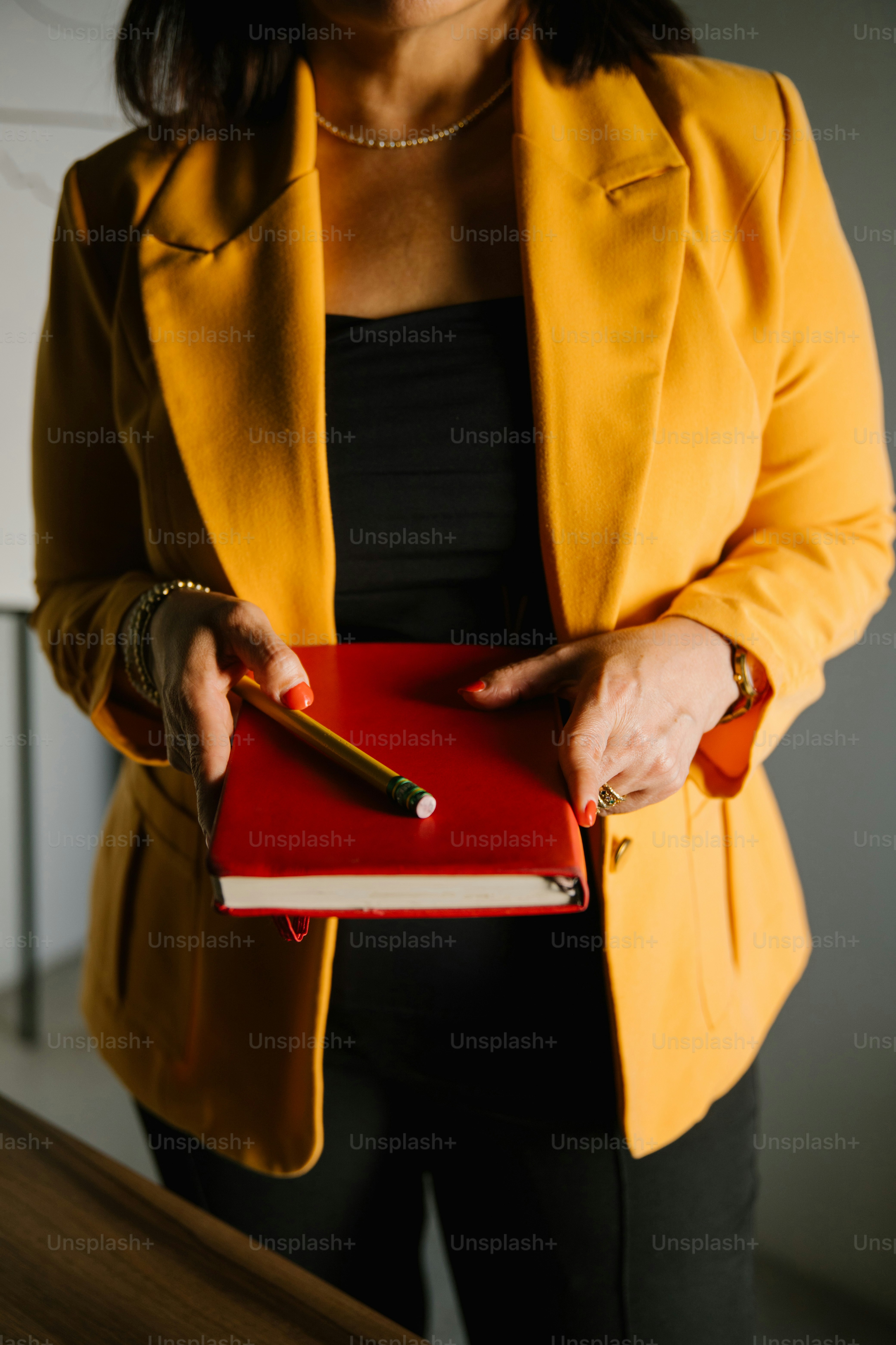Woman in yellow jacket holds a red notebook.
