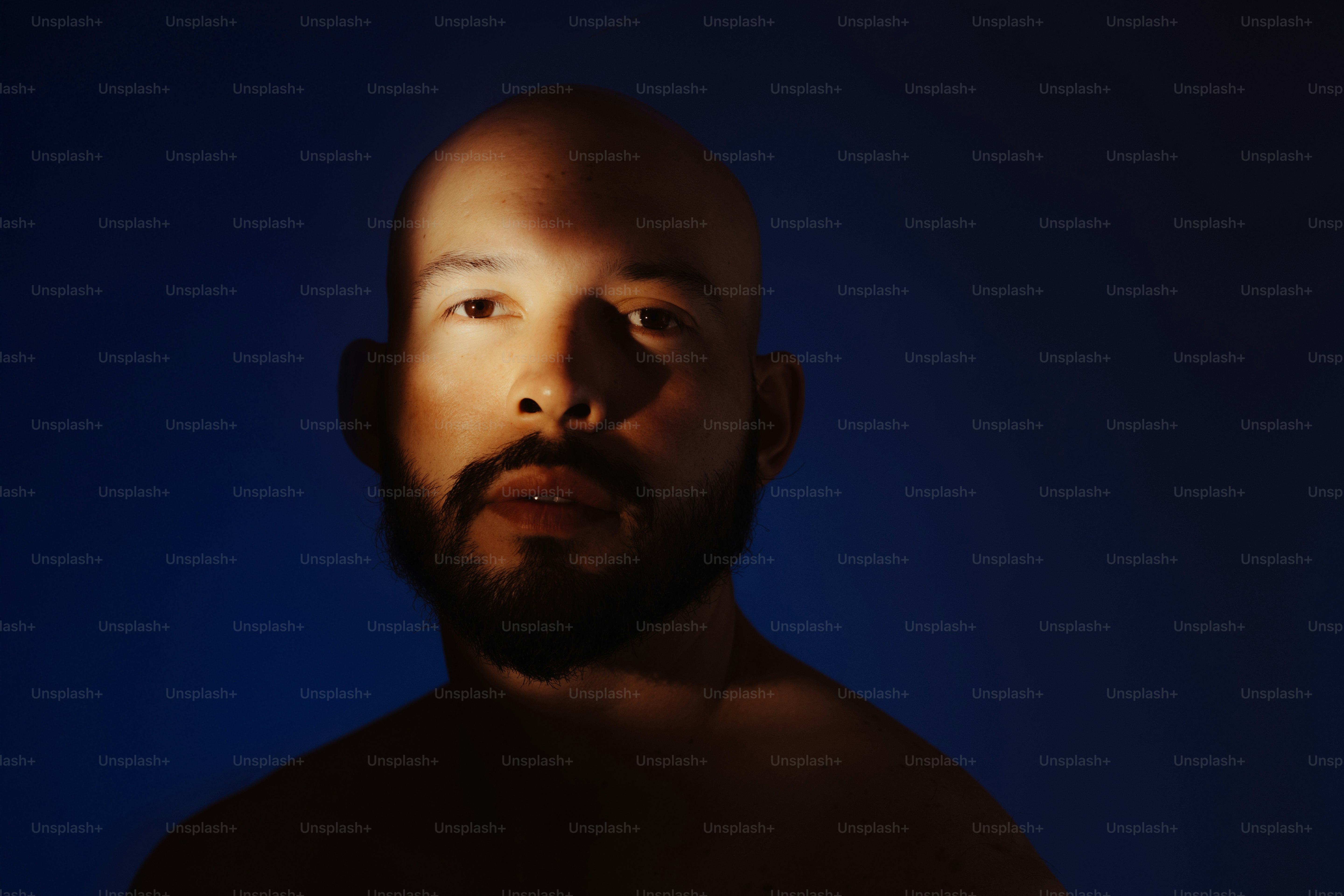 Uomo calvo con barba in illuminazione drammatica.