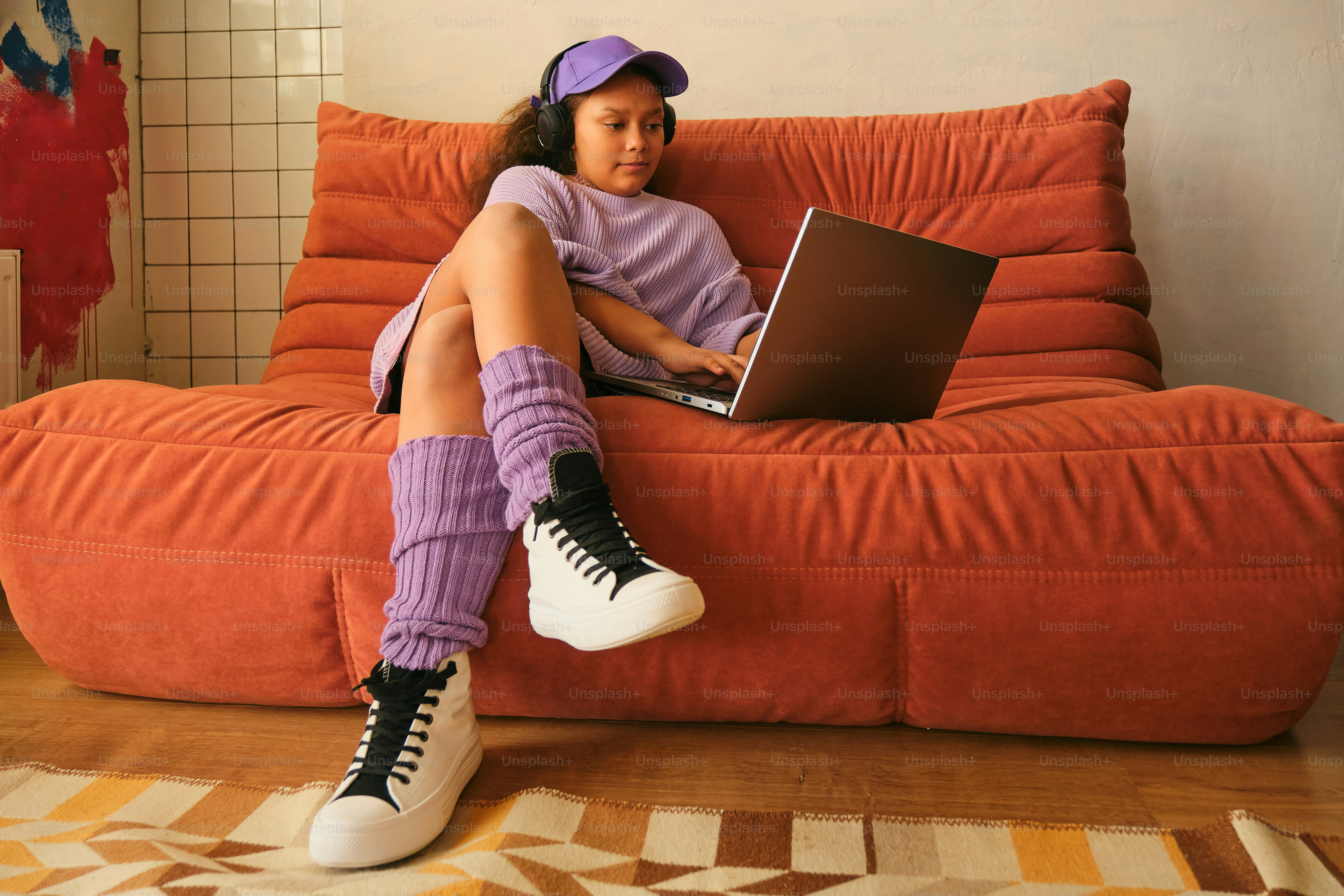Girl using a laptop on an orange couch.