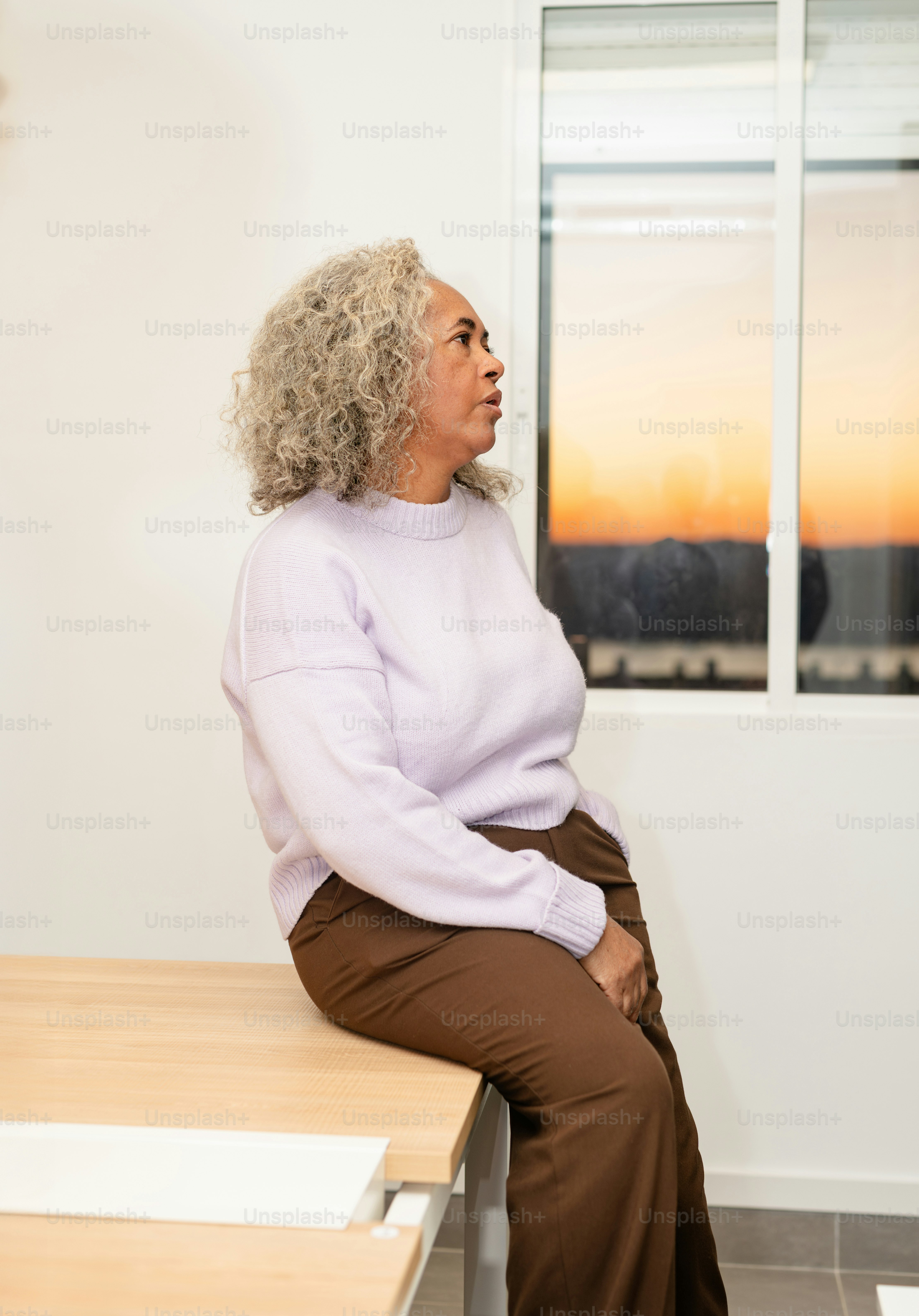 Frau sitzt auf einem Tisch und schaut aus dem Fenster.