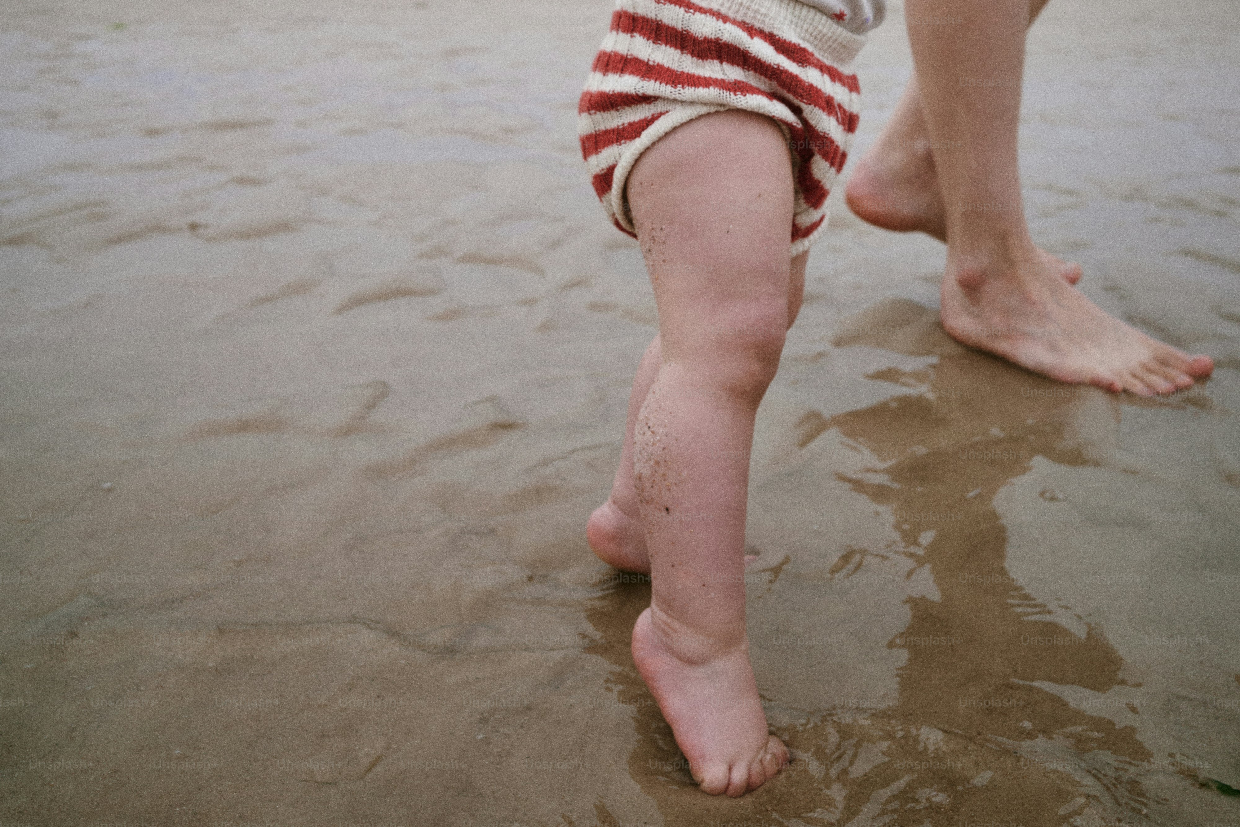 Ein Kind und ein Erwachsener spazieren an einem Sandstrand.