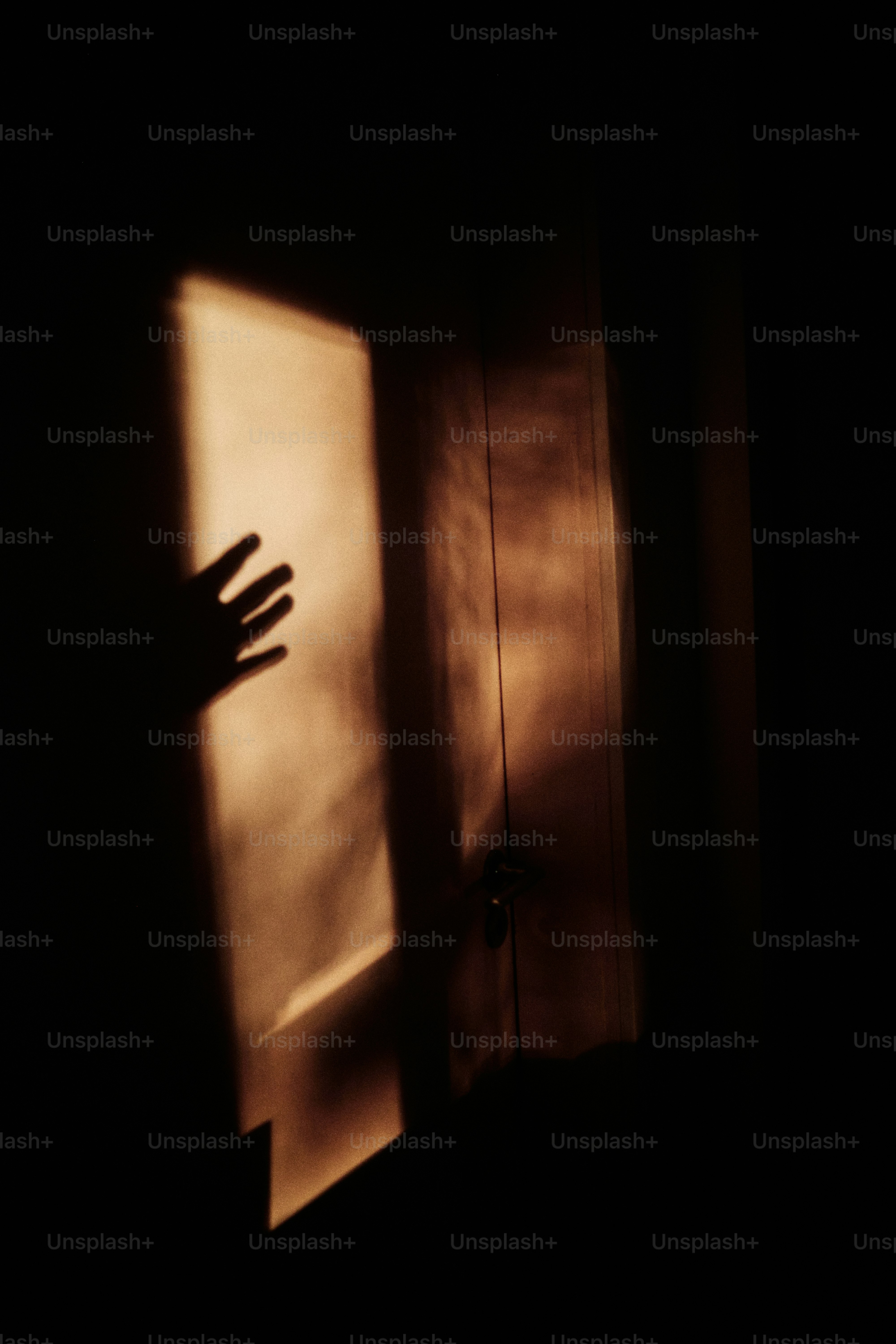 Shadow of hand reaching for sunlight on a door.