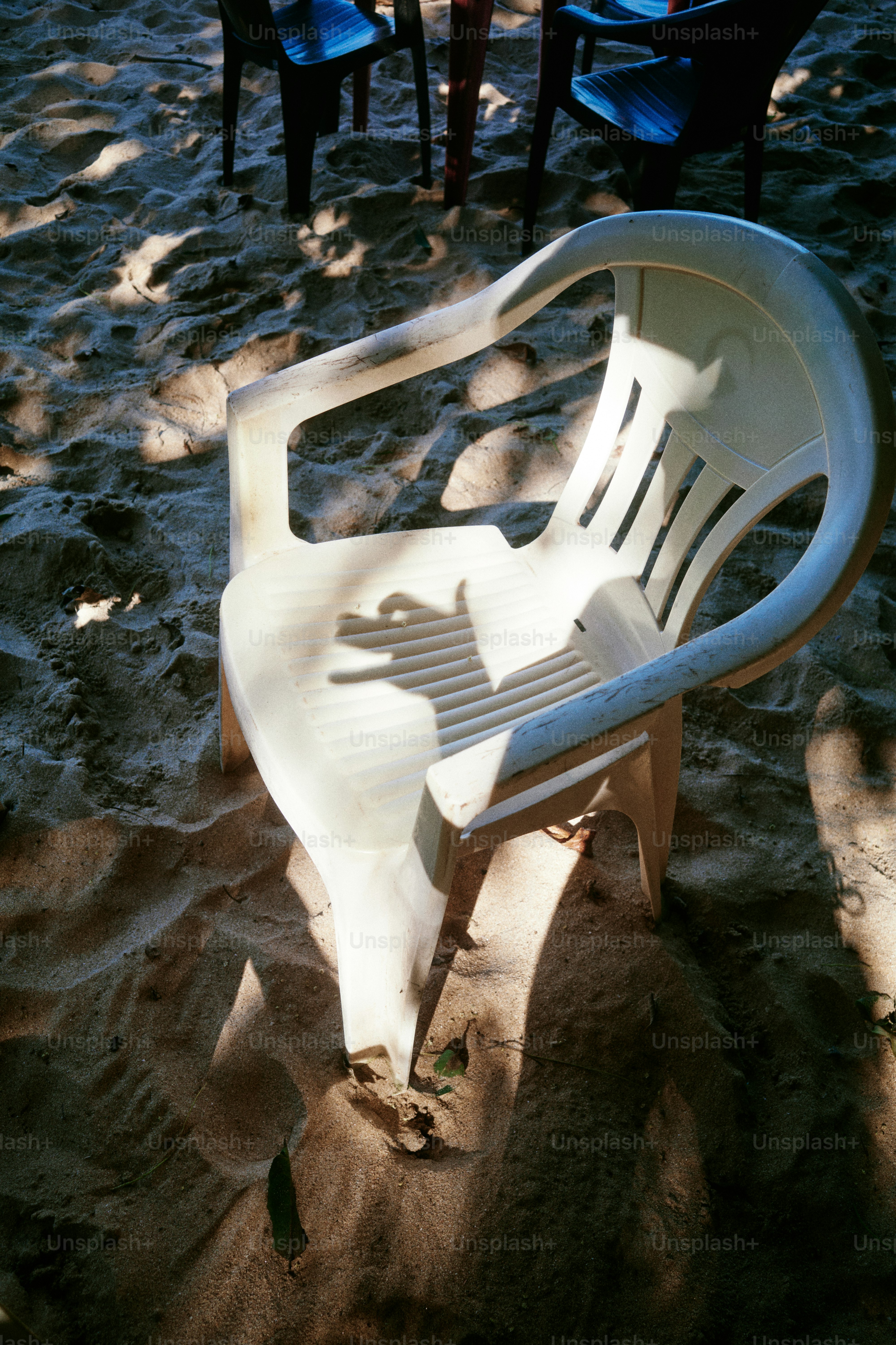 Ein weißer Plastikstuhl ruht auf dem Sand.