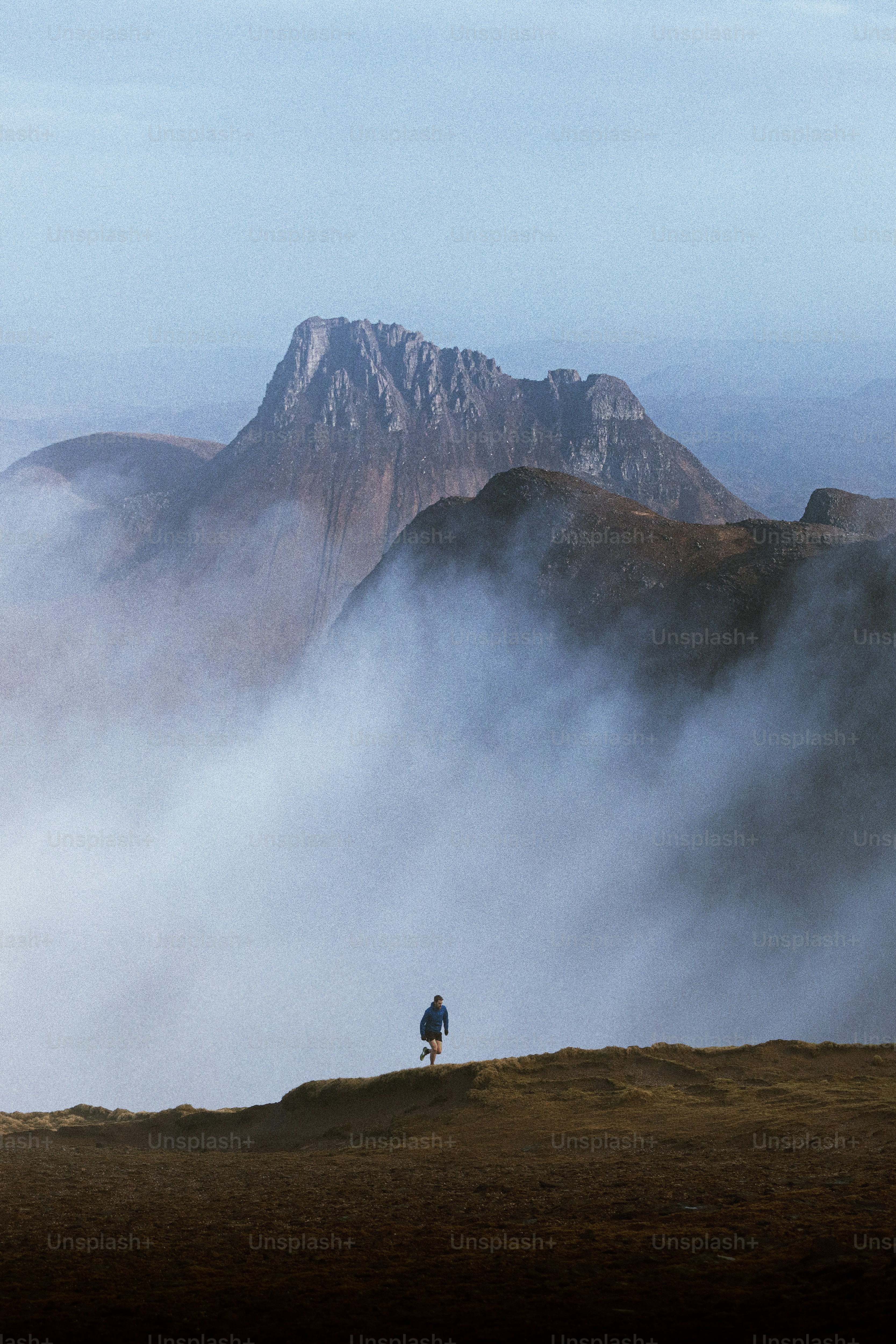A hiker strolls toward mountains through fog.