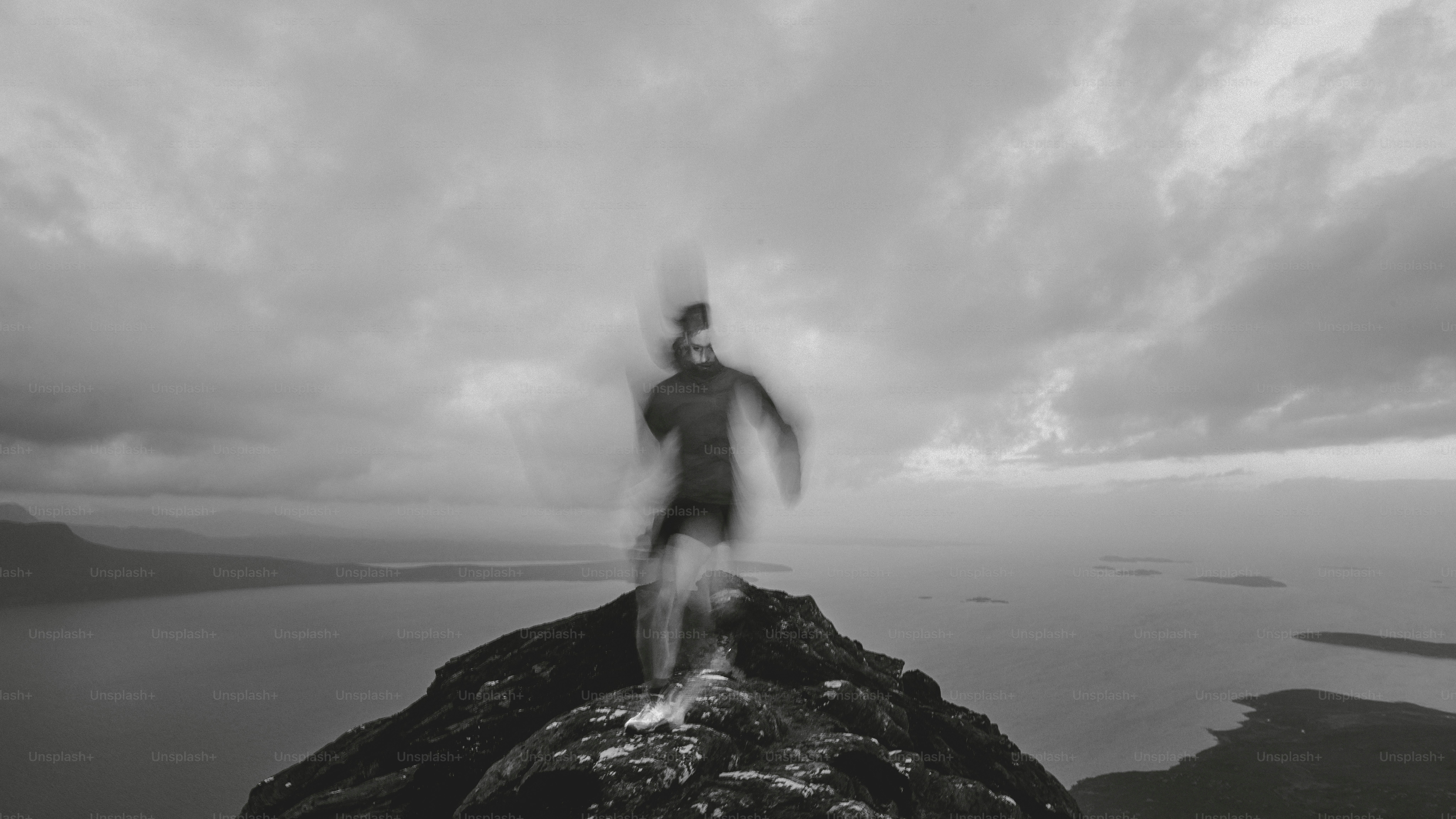 Runner on a peak, blurred against a cloudy sky.