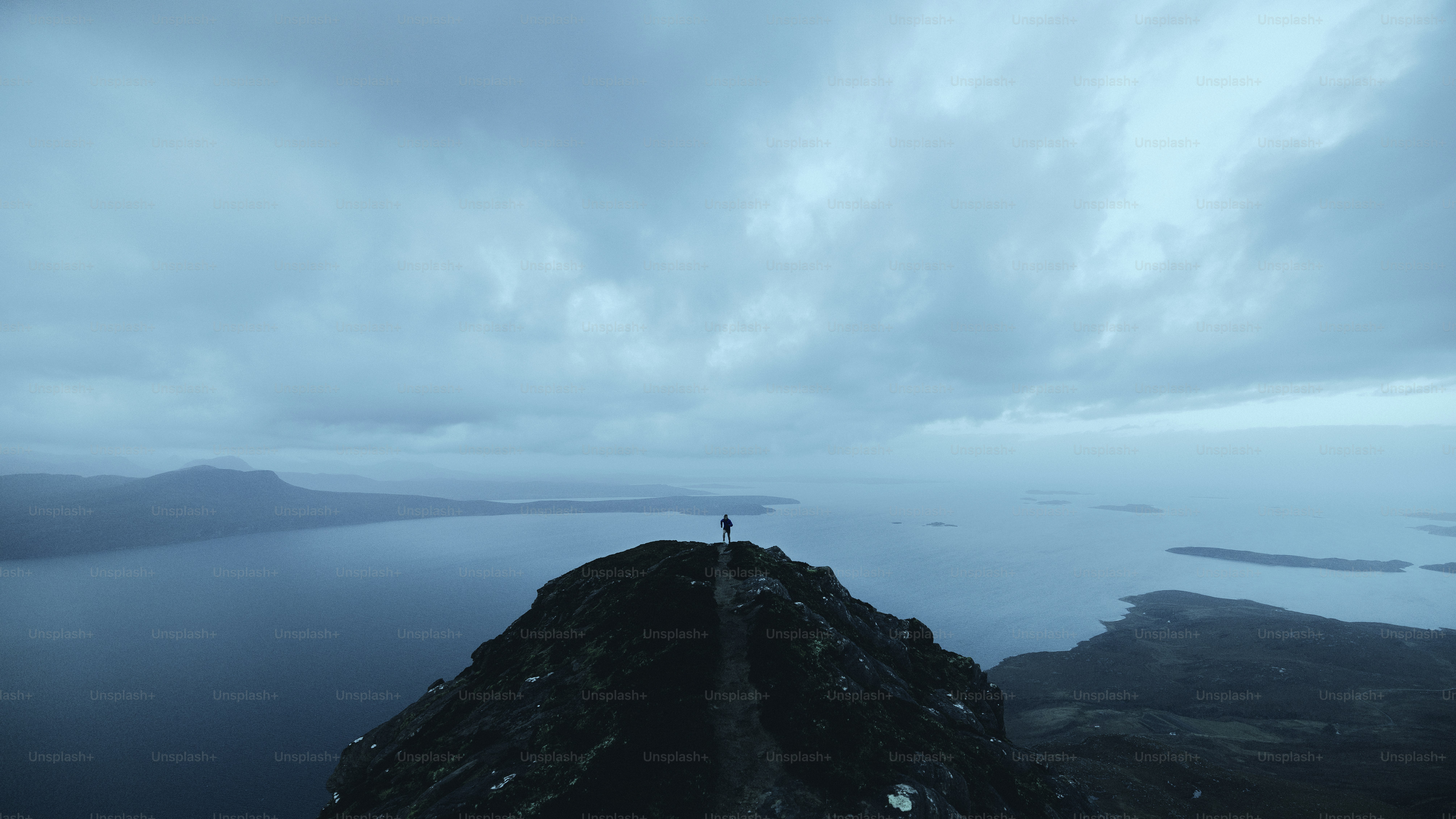 A person stands atop a mountain overlooking a sea.