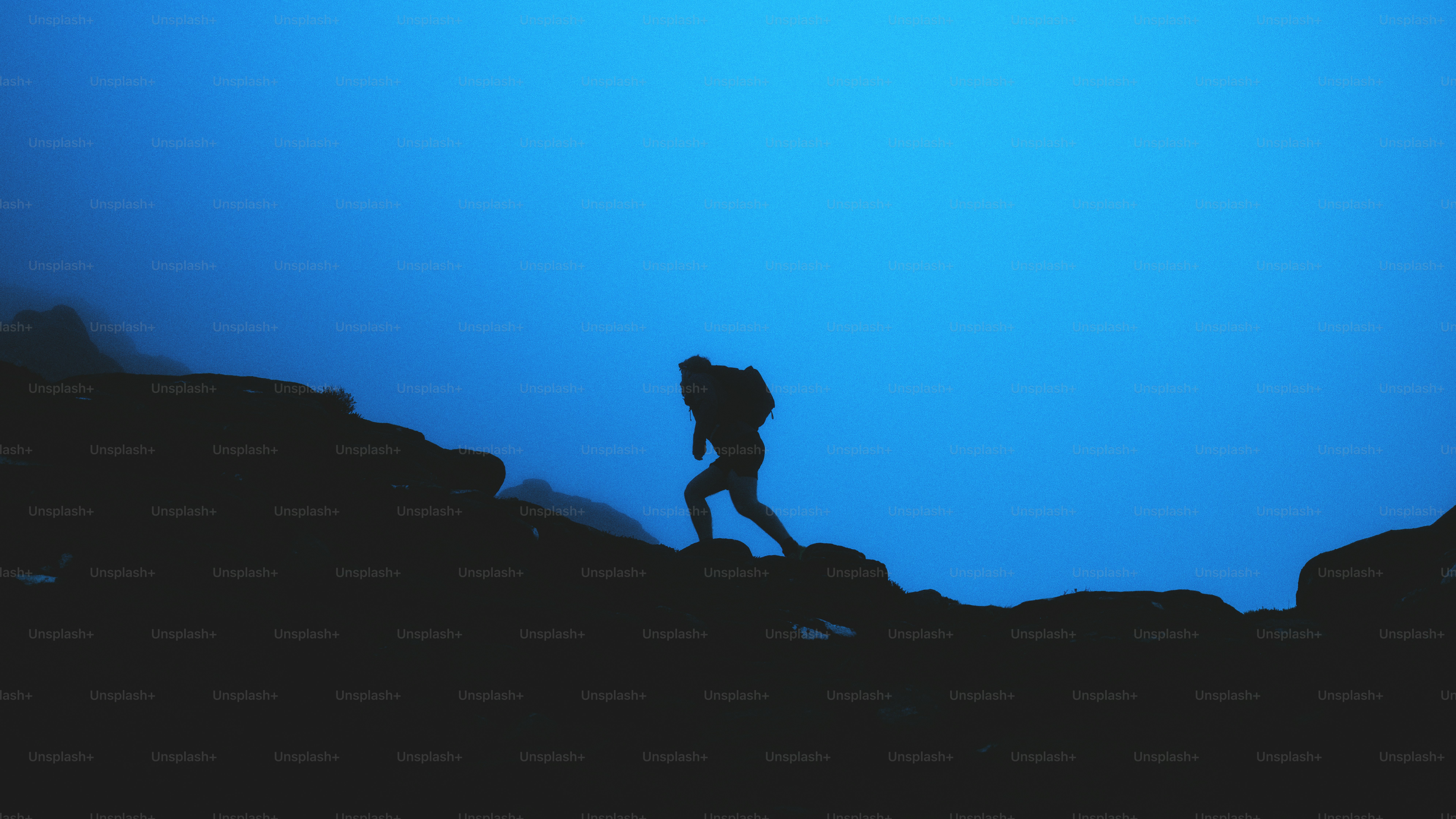 Hiker's silhouette climbs upward against blue sky.