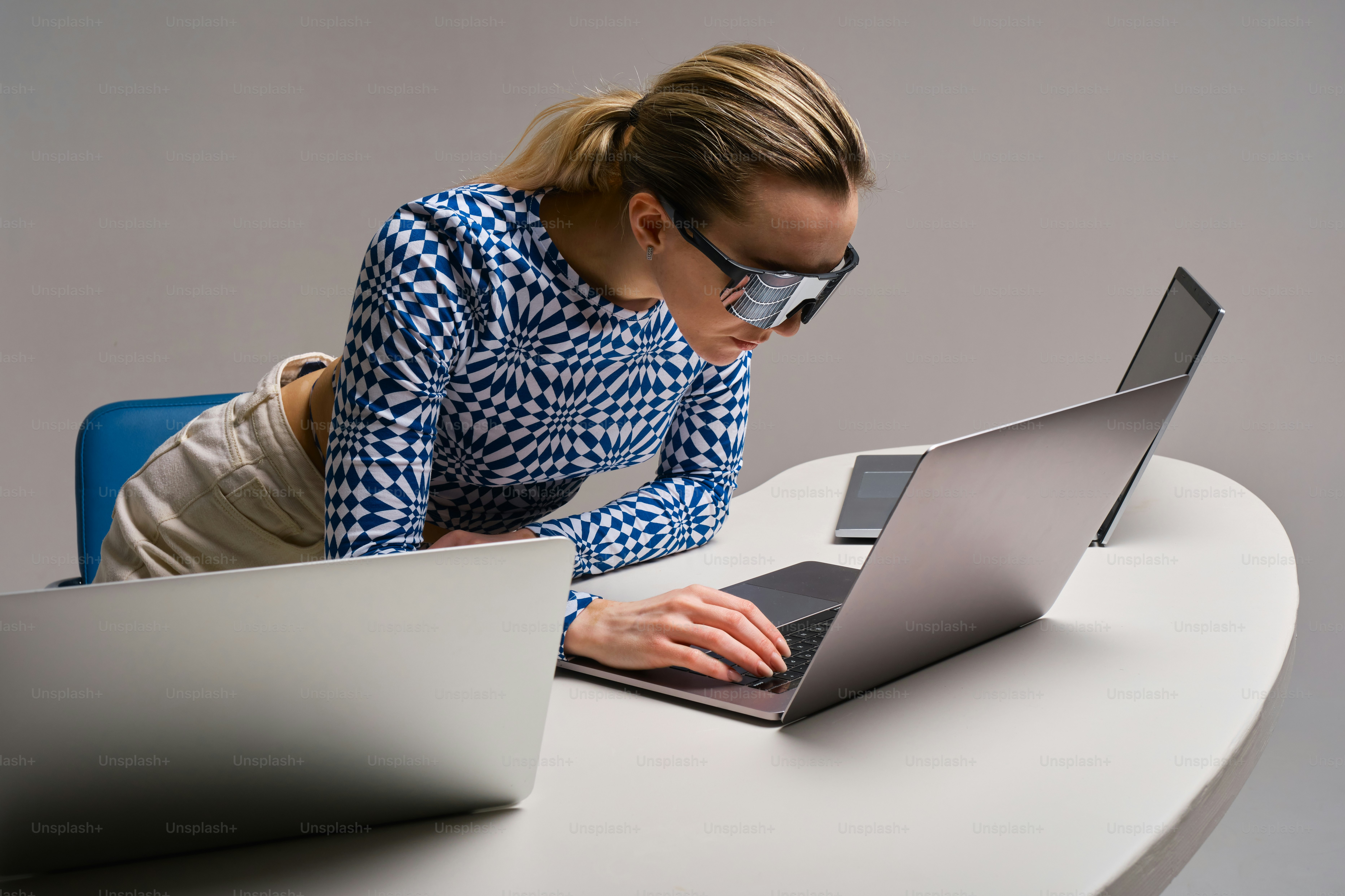 Woman works intently on multiple laptops.