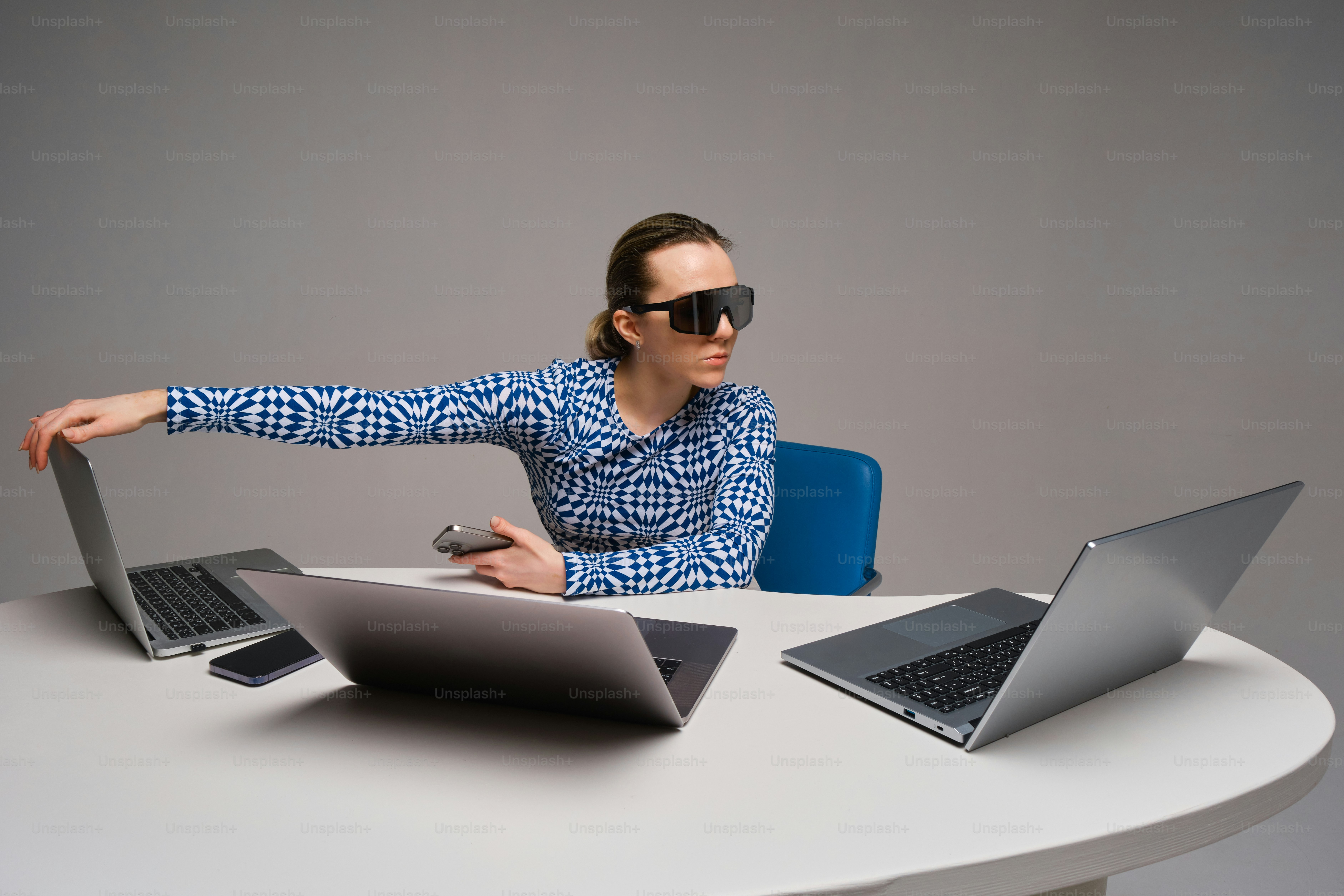 Person with sunglasses surrounded by three laptops.