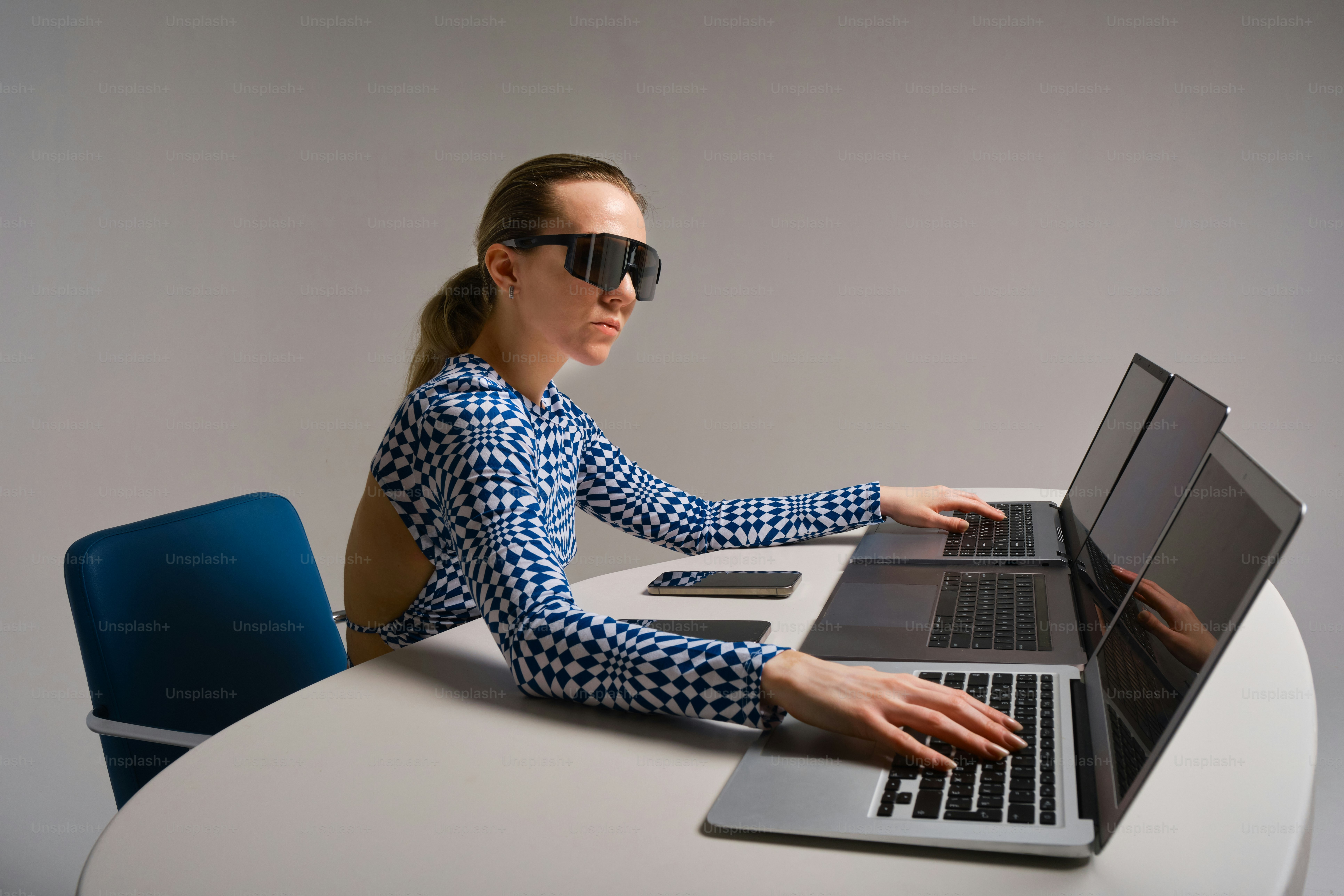 A woman works on laptops, focused and intense.