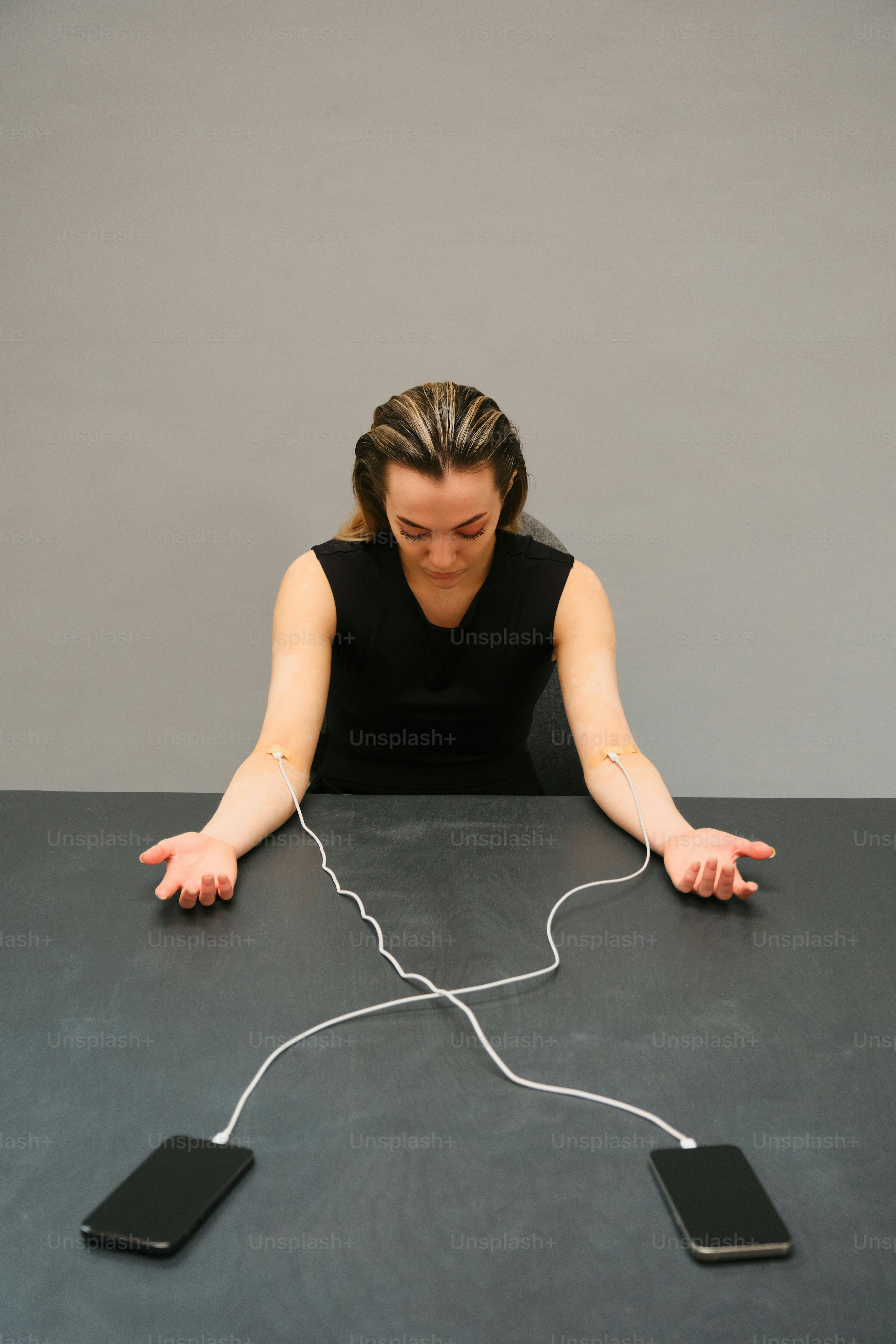 Woman's arms connected to phones with charging cords.