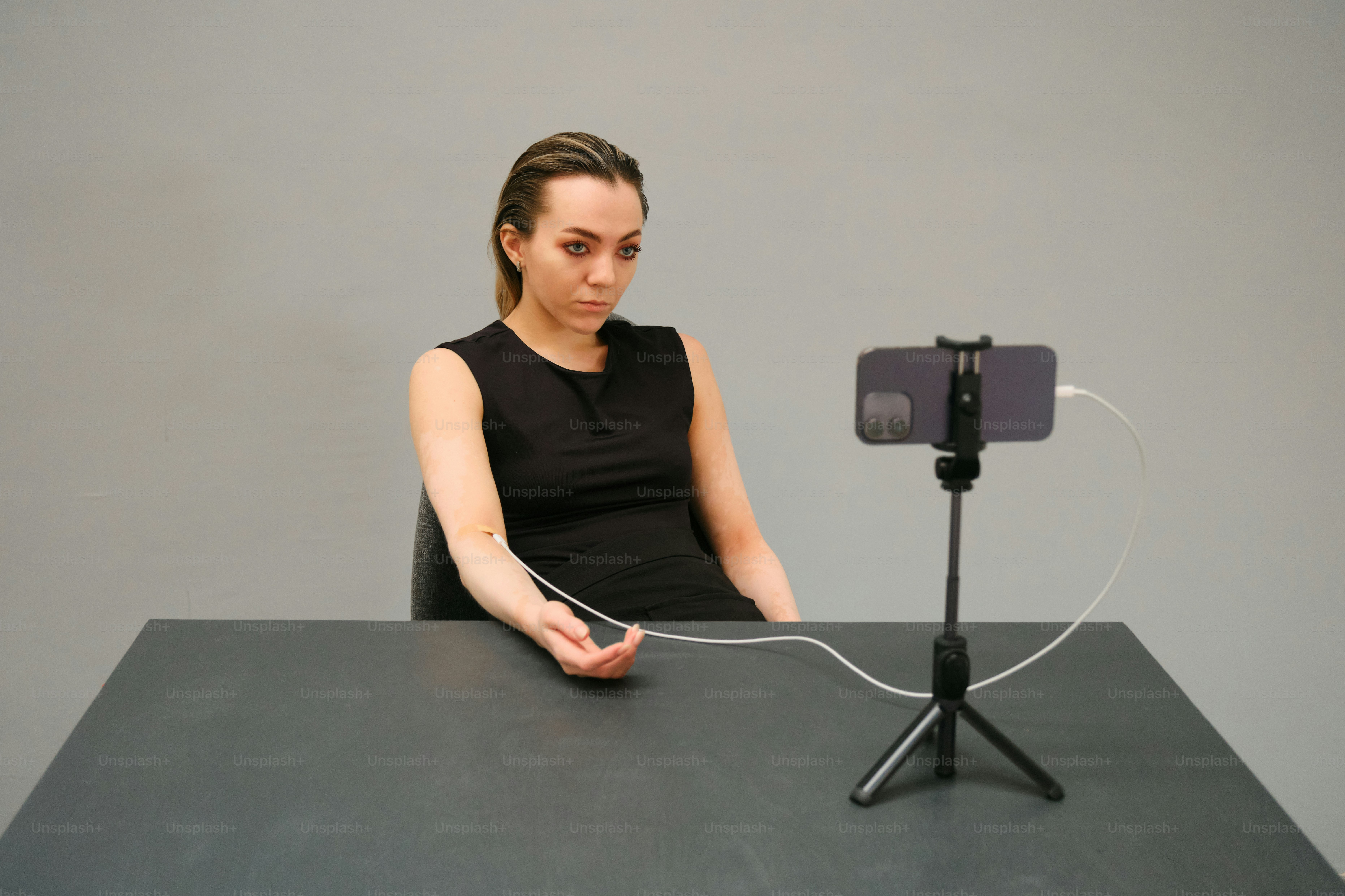 Woman sits at a desk with a smartphone and wire.