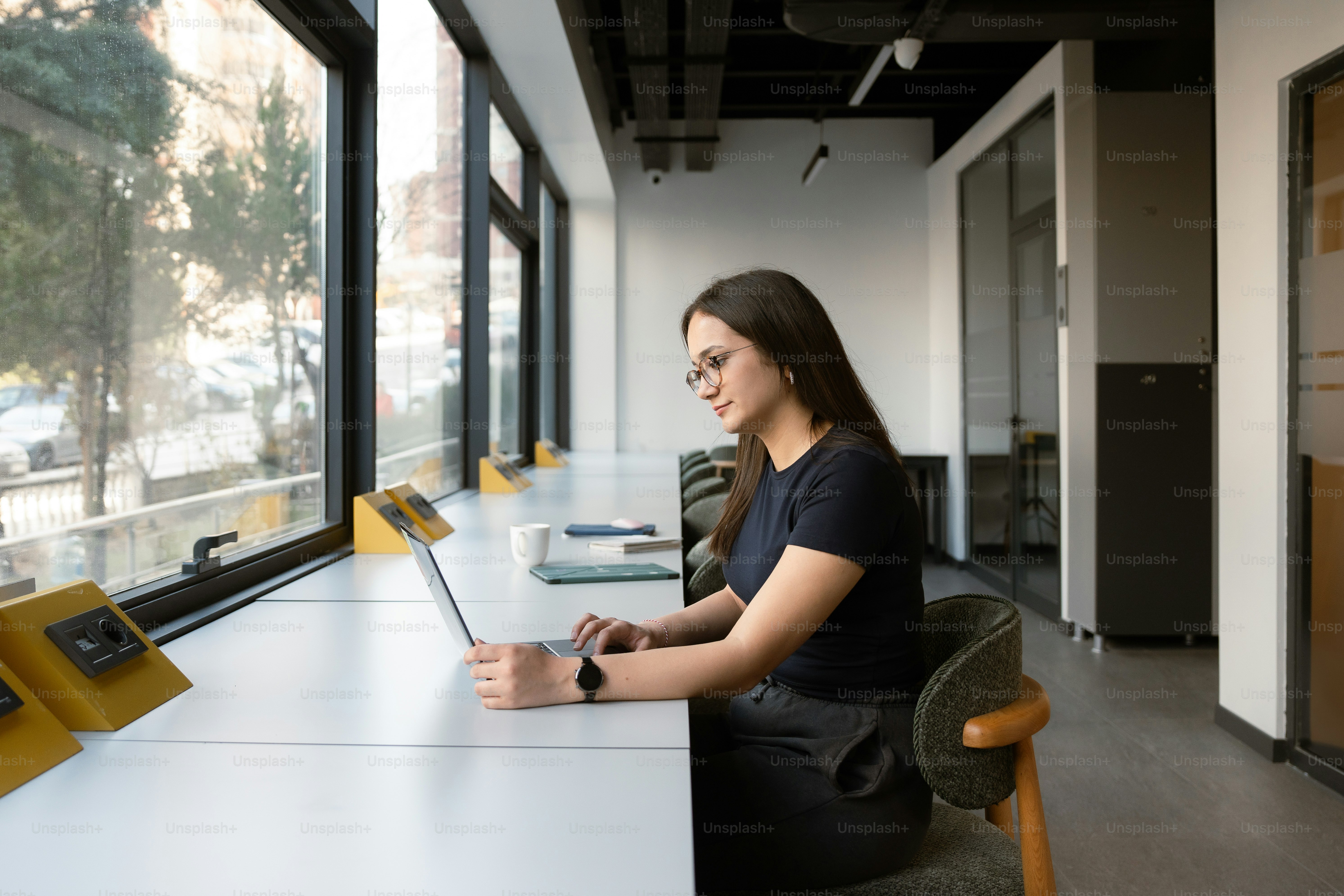 Woman is working on a laptop by a window.