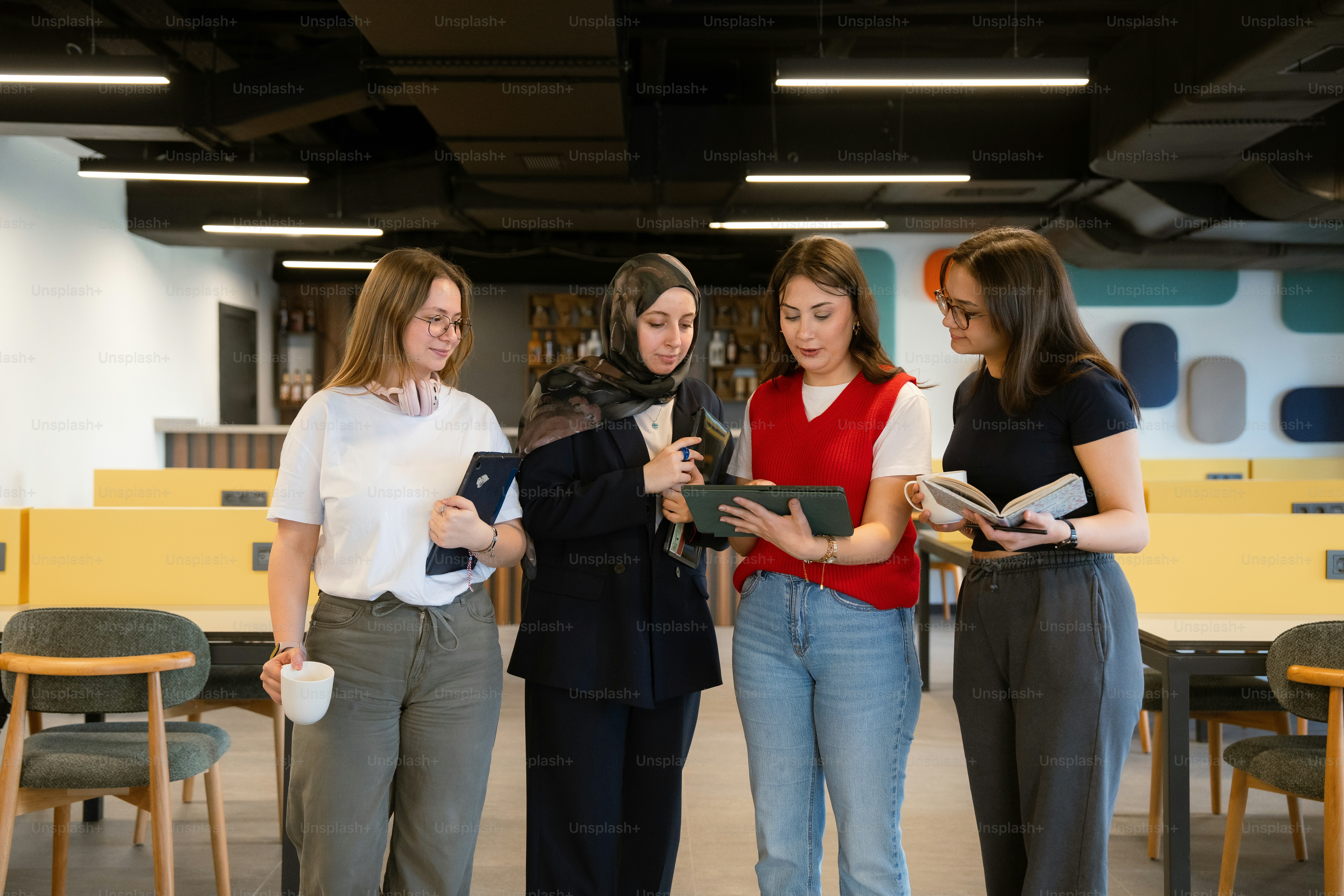 Four women look at a phone in a modern office.