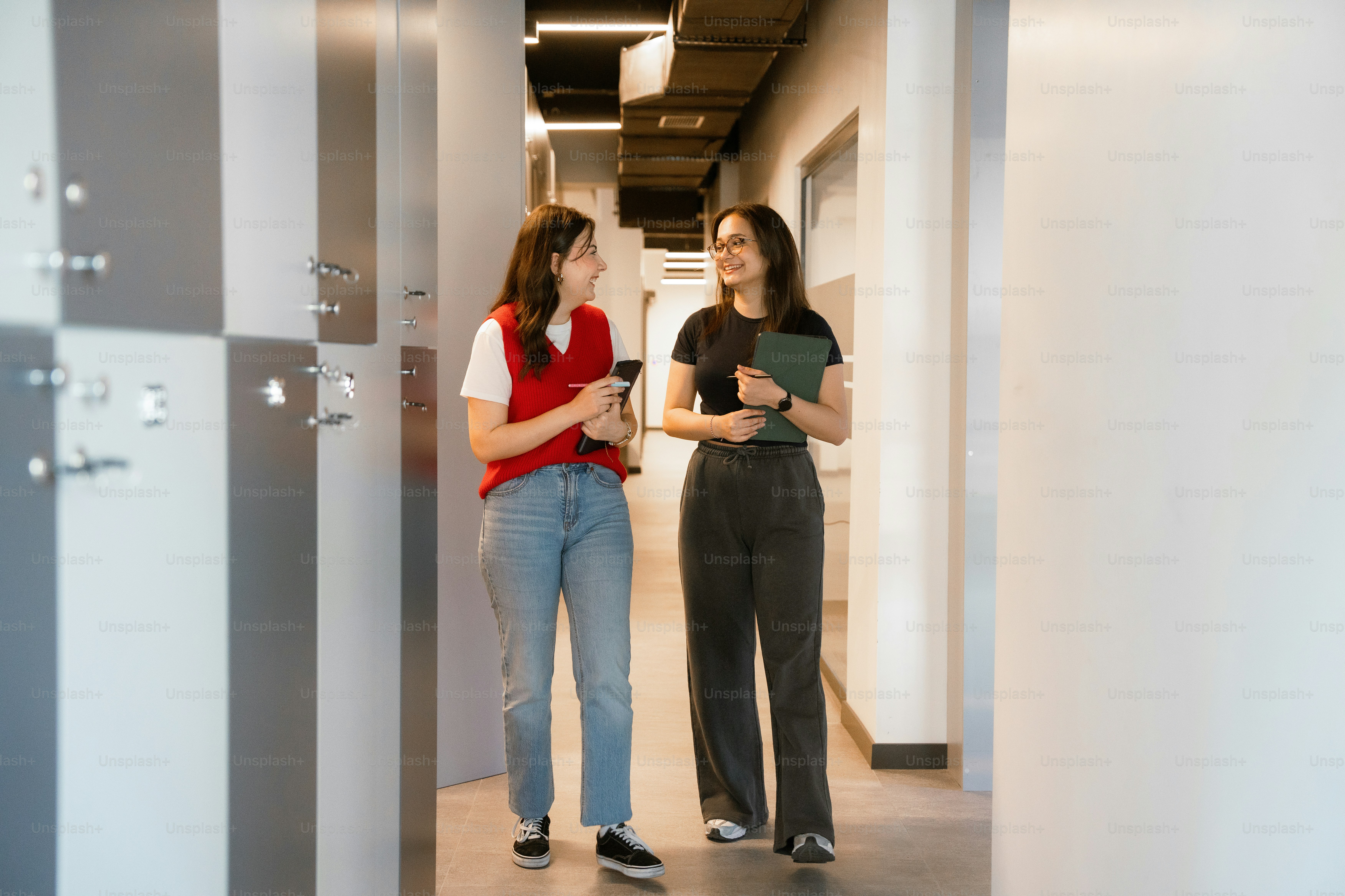 Two women are walking and talking in a hallway.