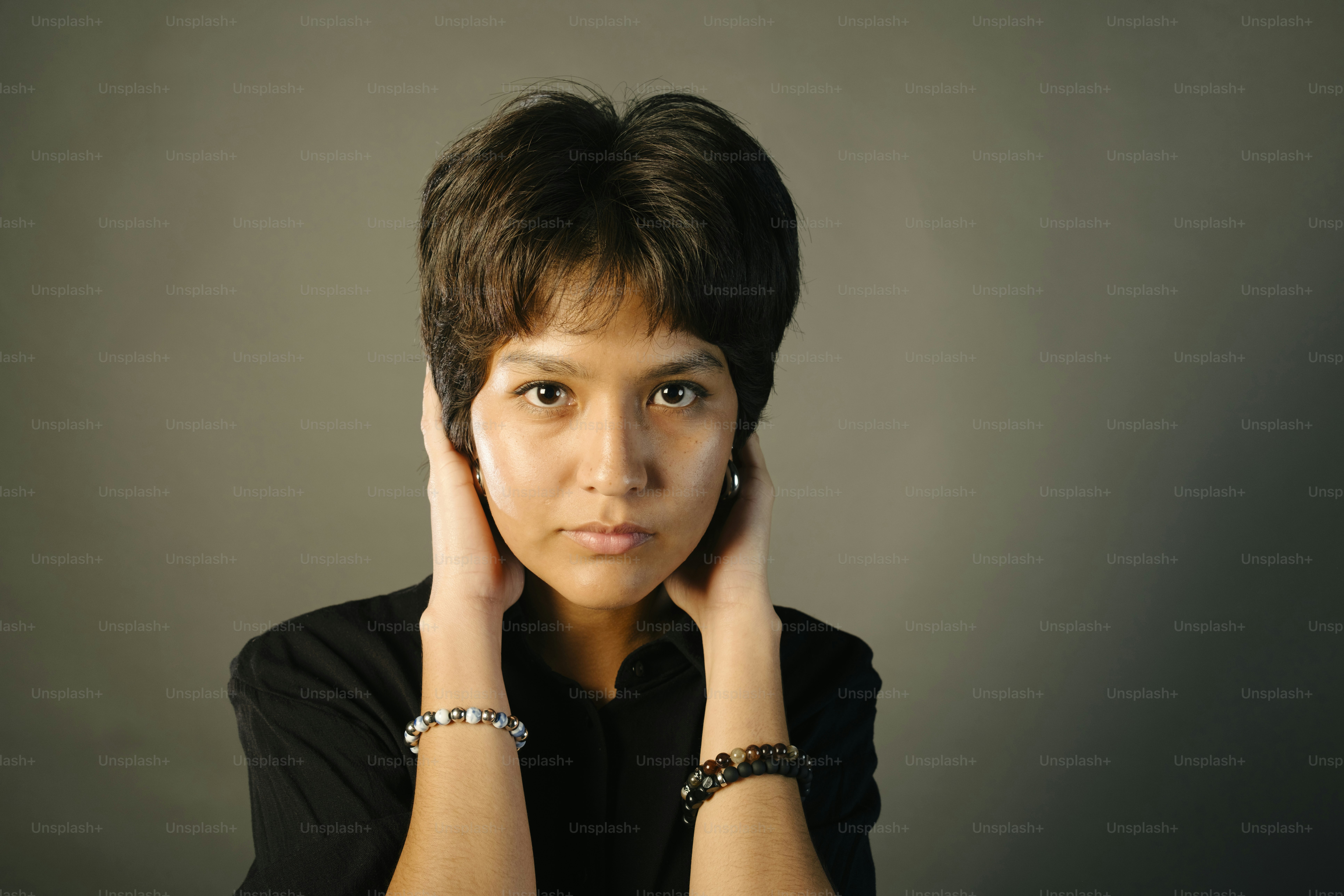 Woman covers her ears with hands, looking at camera