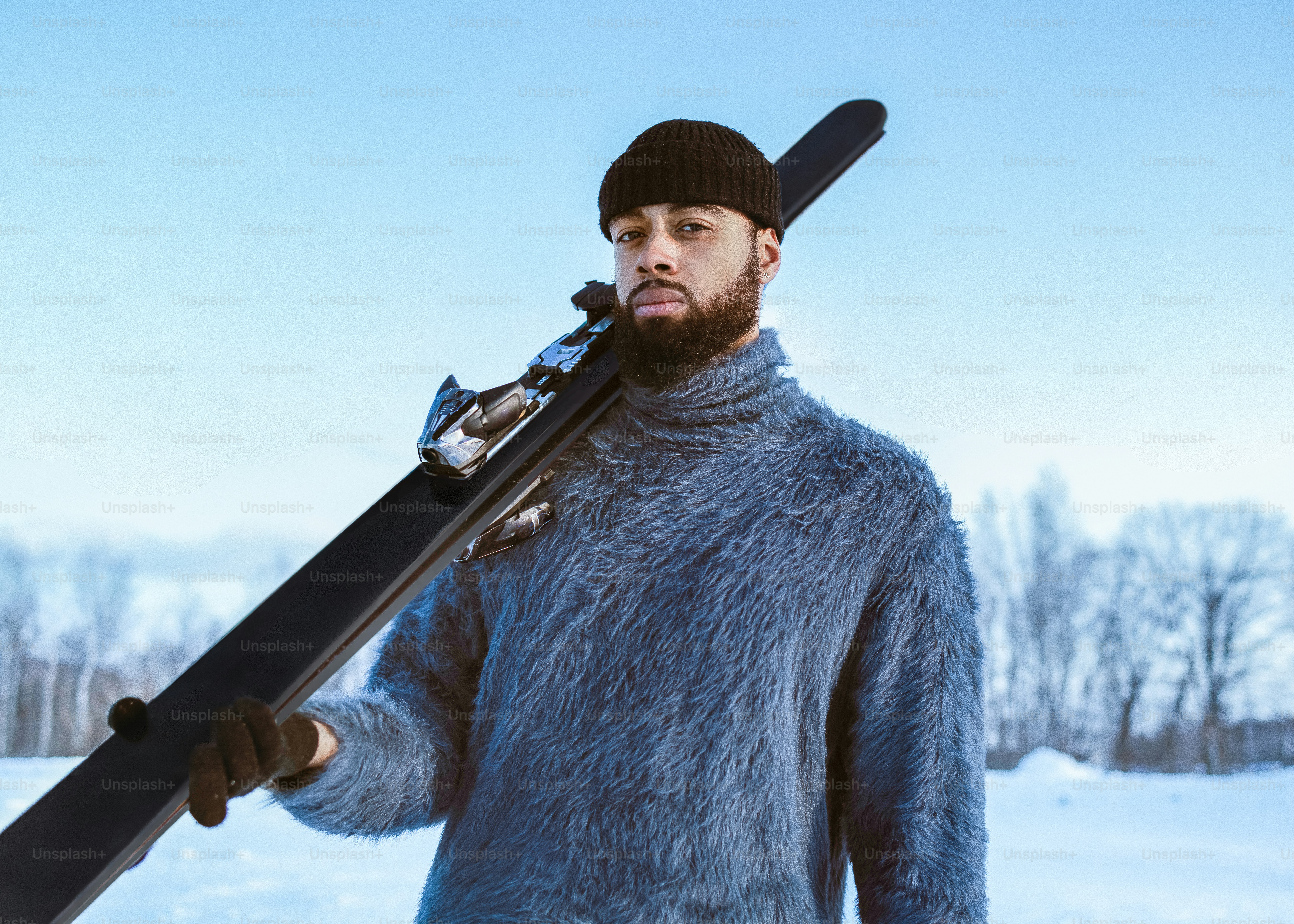 Man in winter clothes holds skis on his shoulder.