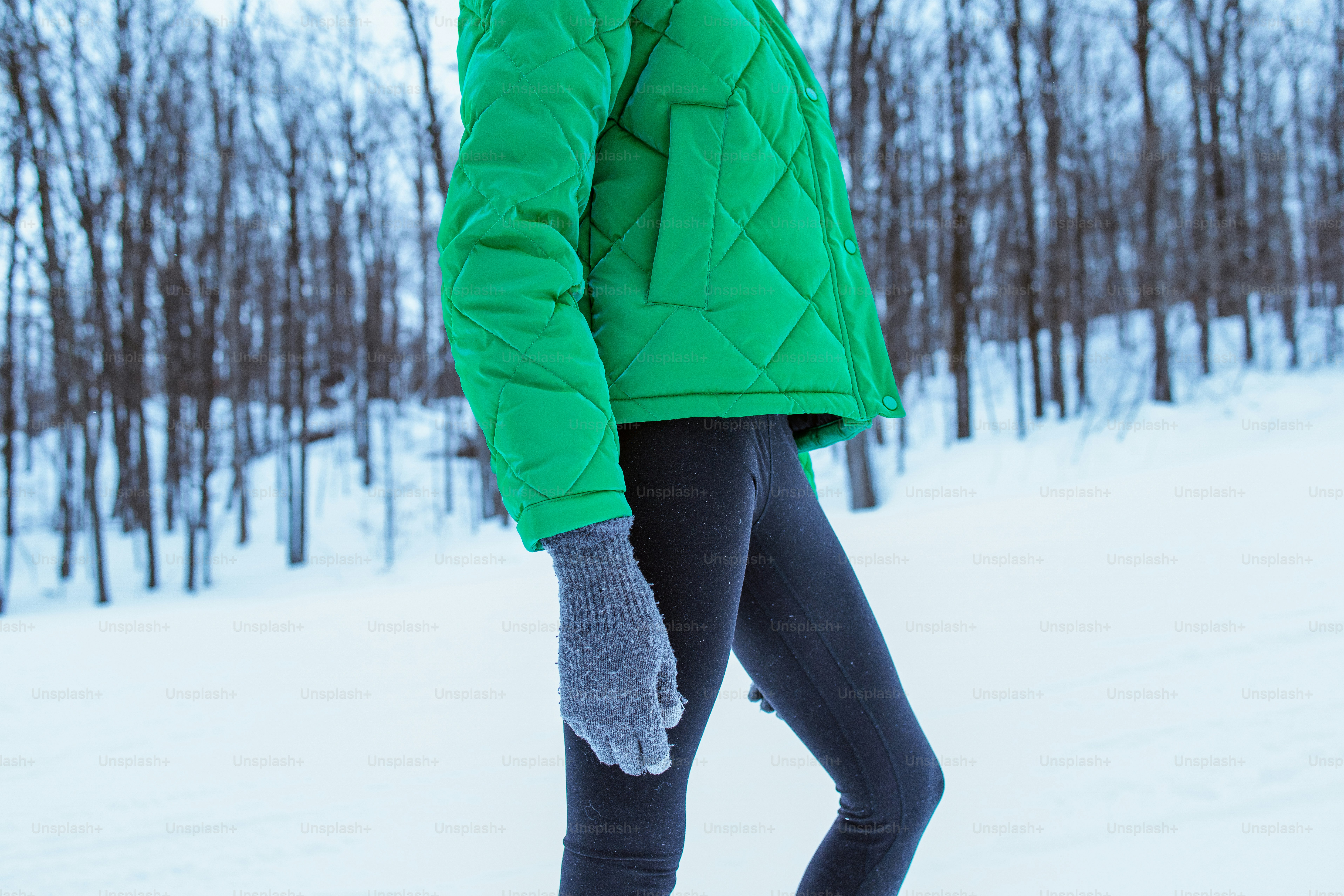 Woman in green jacket and leggings walks in snow.