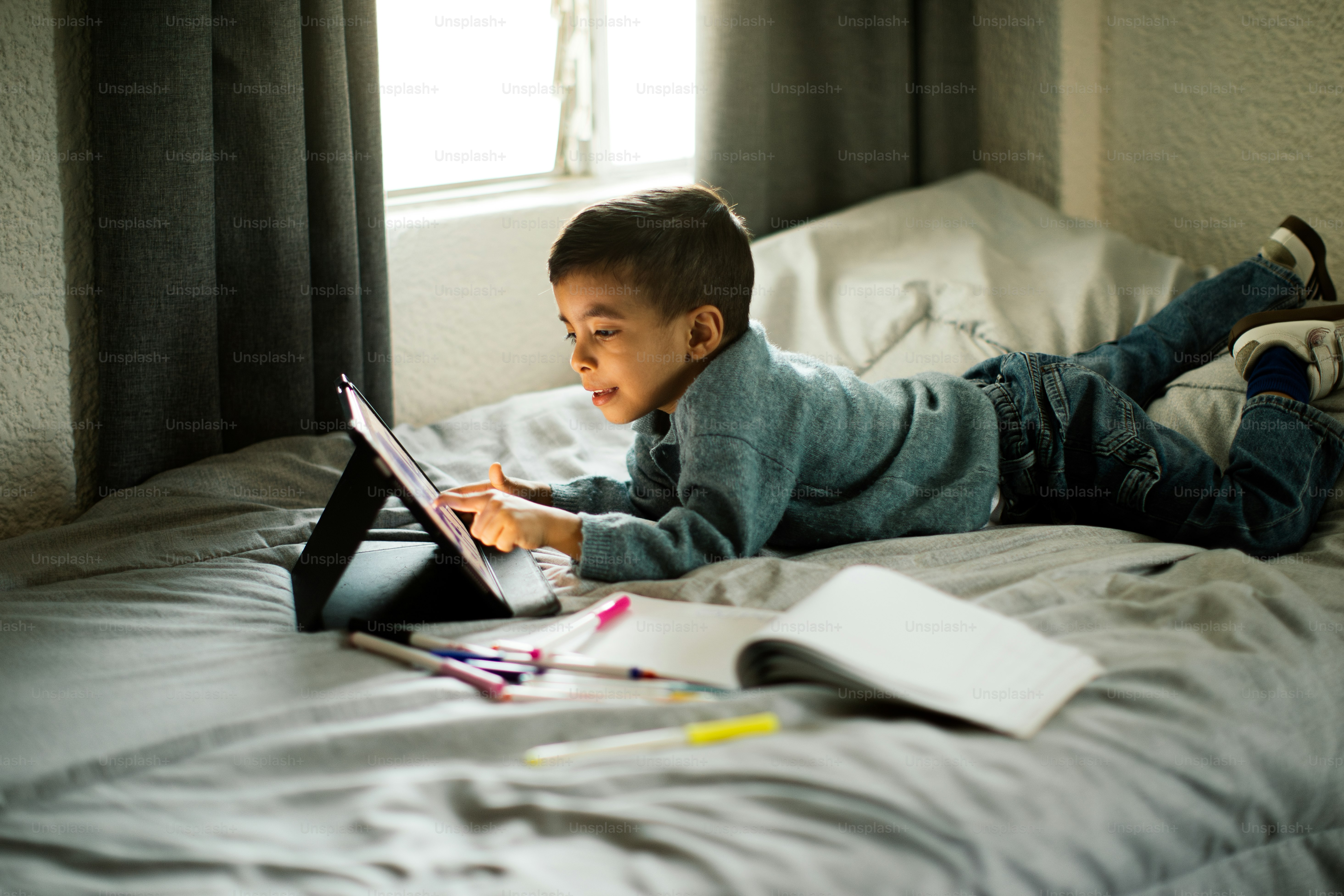 Un garçon utilise une tablette sur son lit.