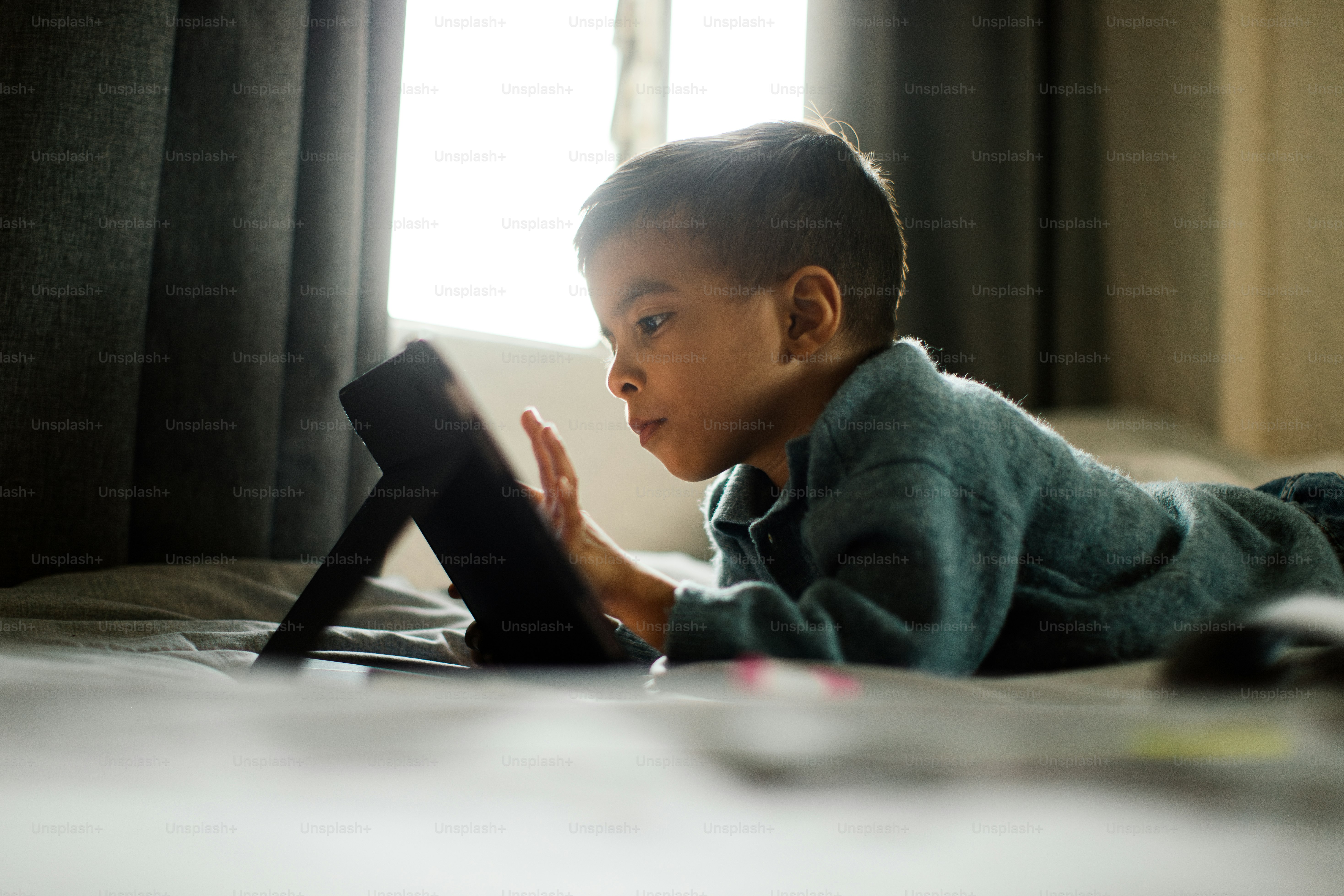 A child is laying on a bed, using a tablet.