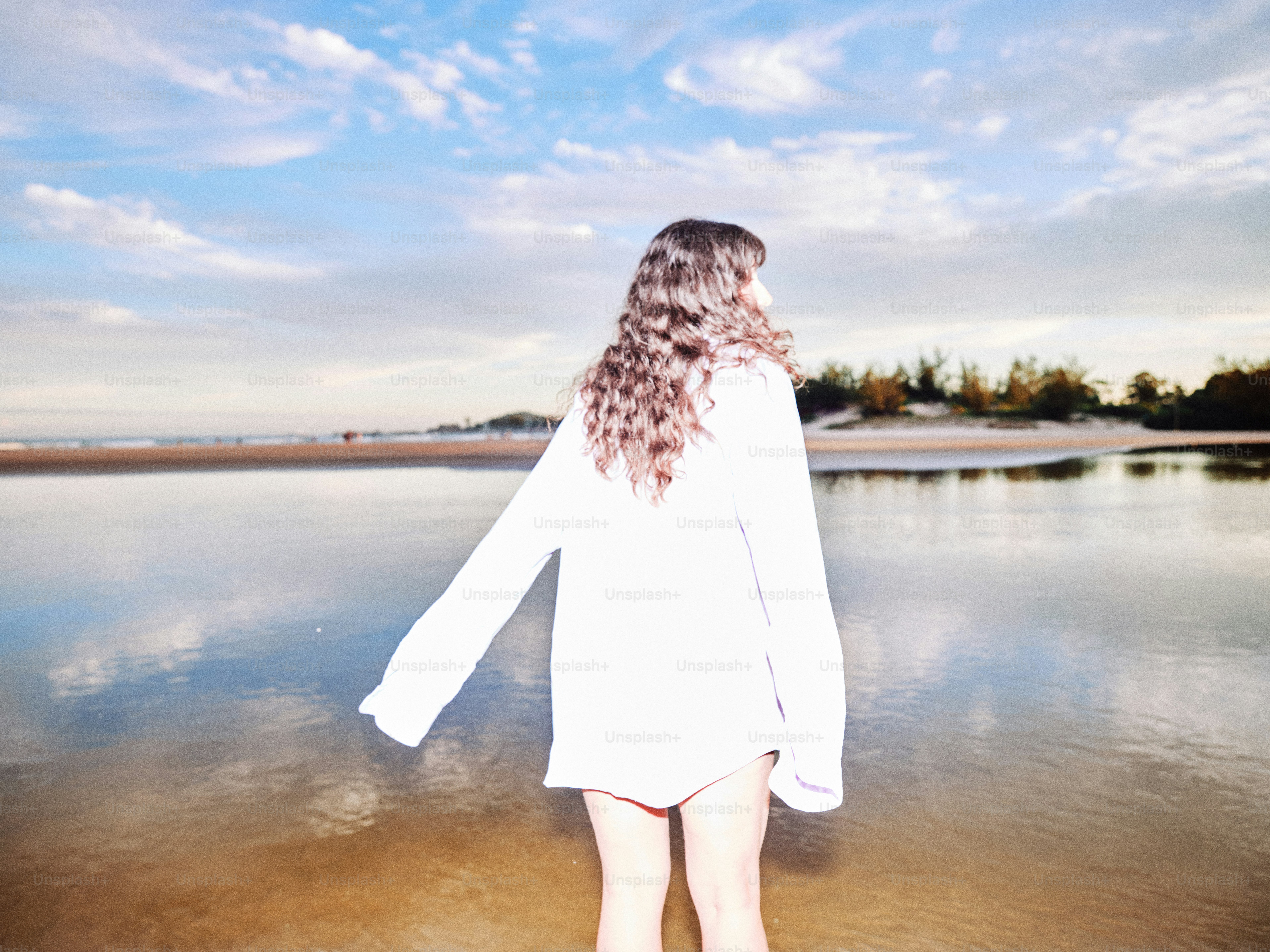 Woman stands in the water, facing the horizon.