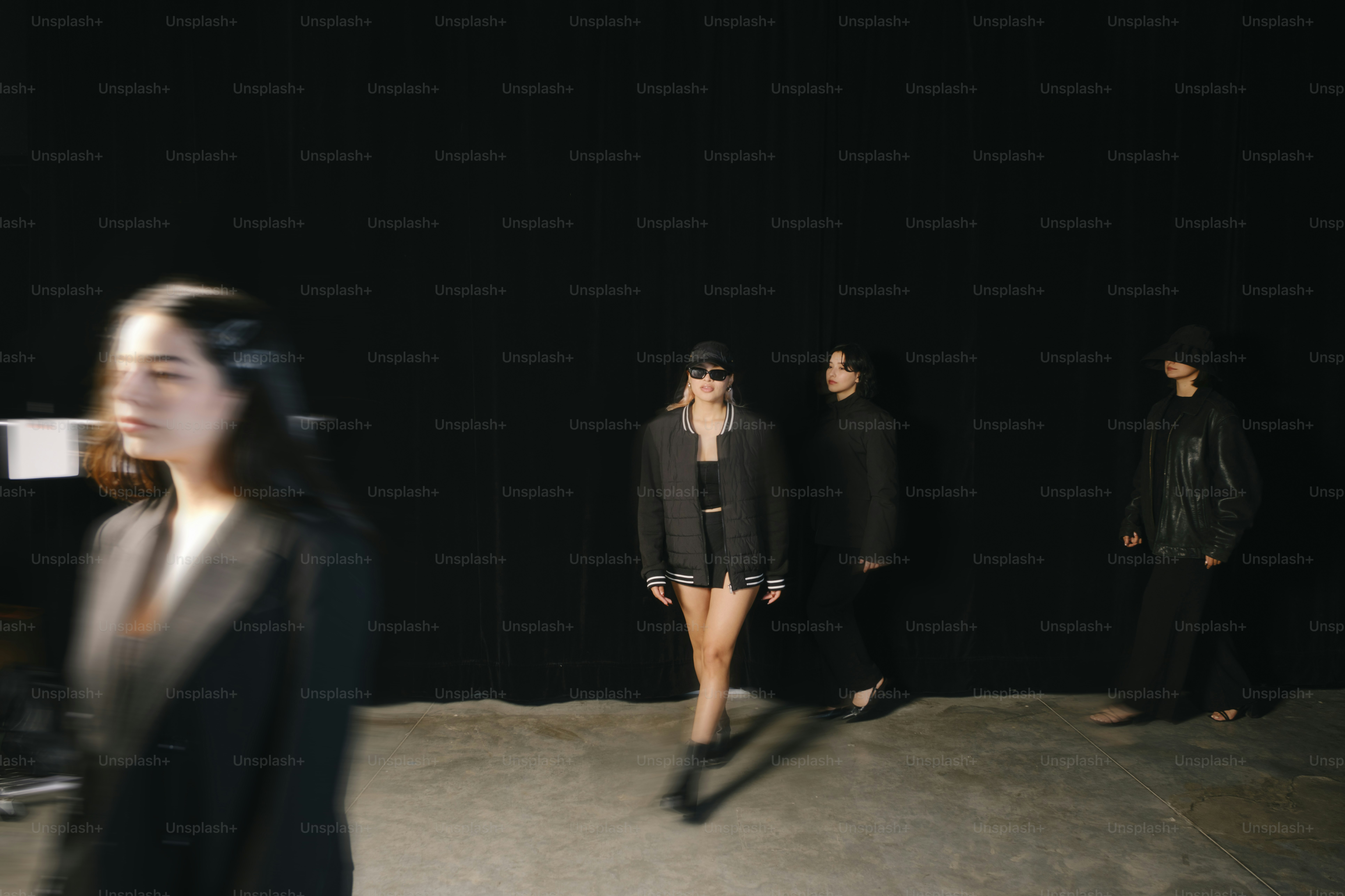 Women are walking on a runway in dark clothing.