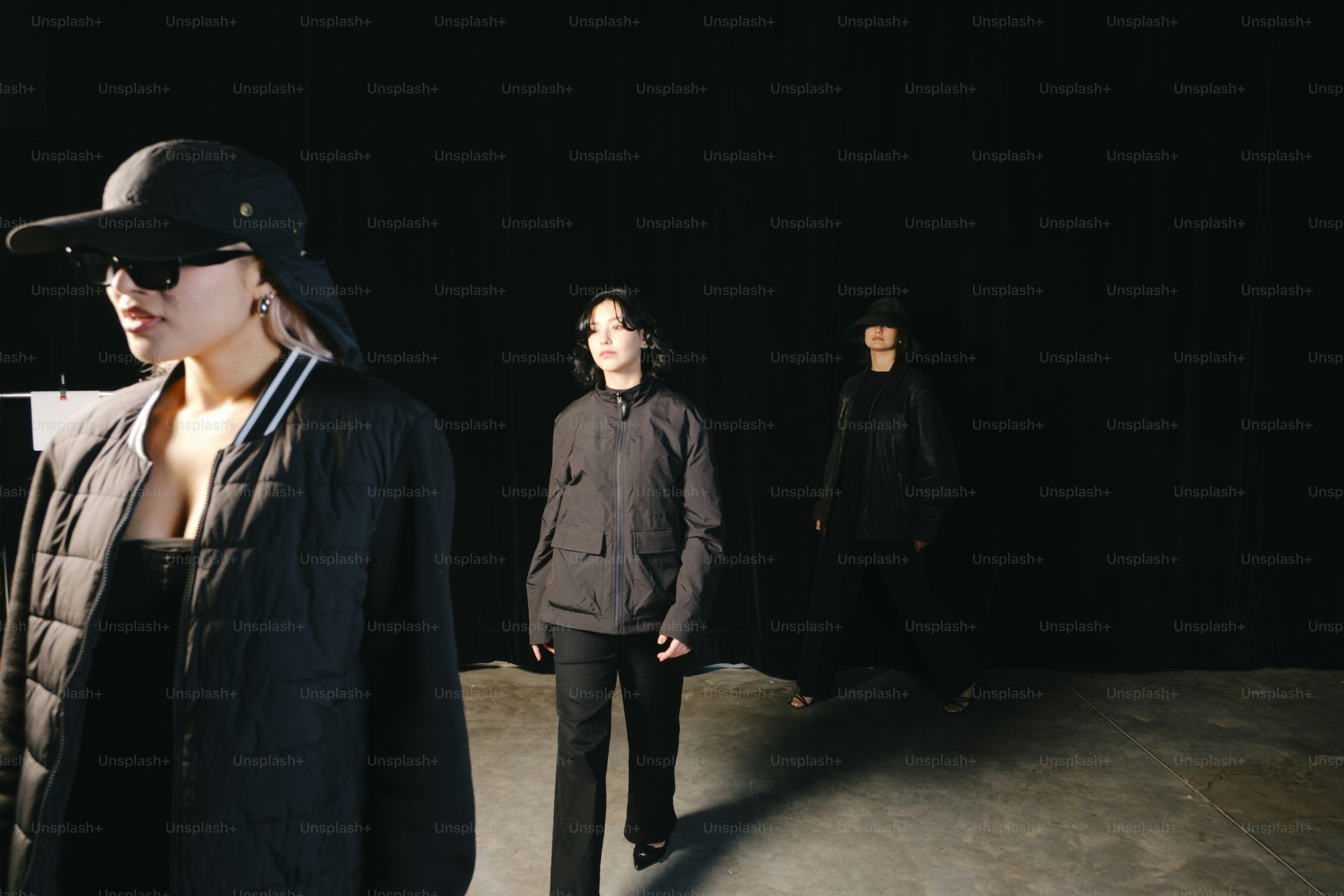 Three people wear black clothing in the darkness.