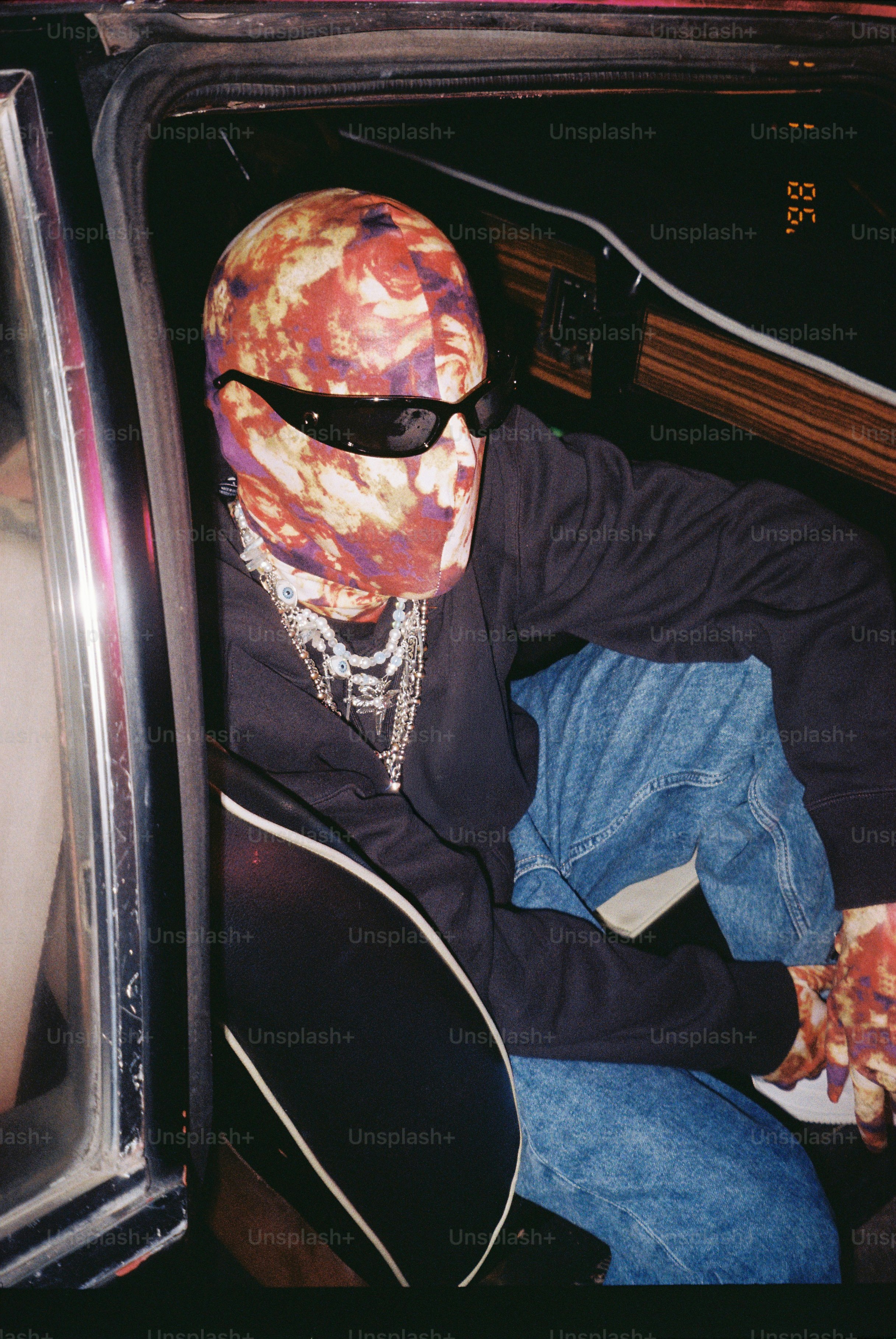 Person wearing a mask and sunglasses sits in a car.