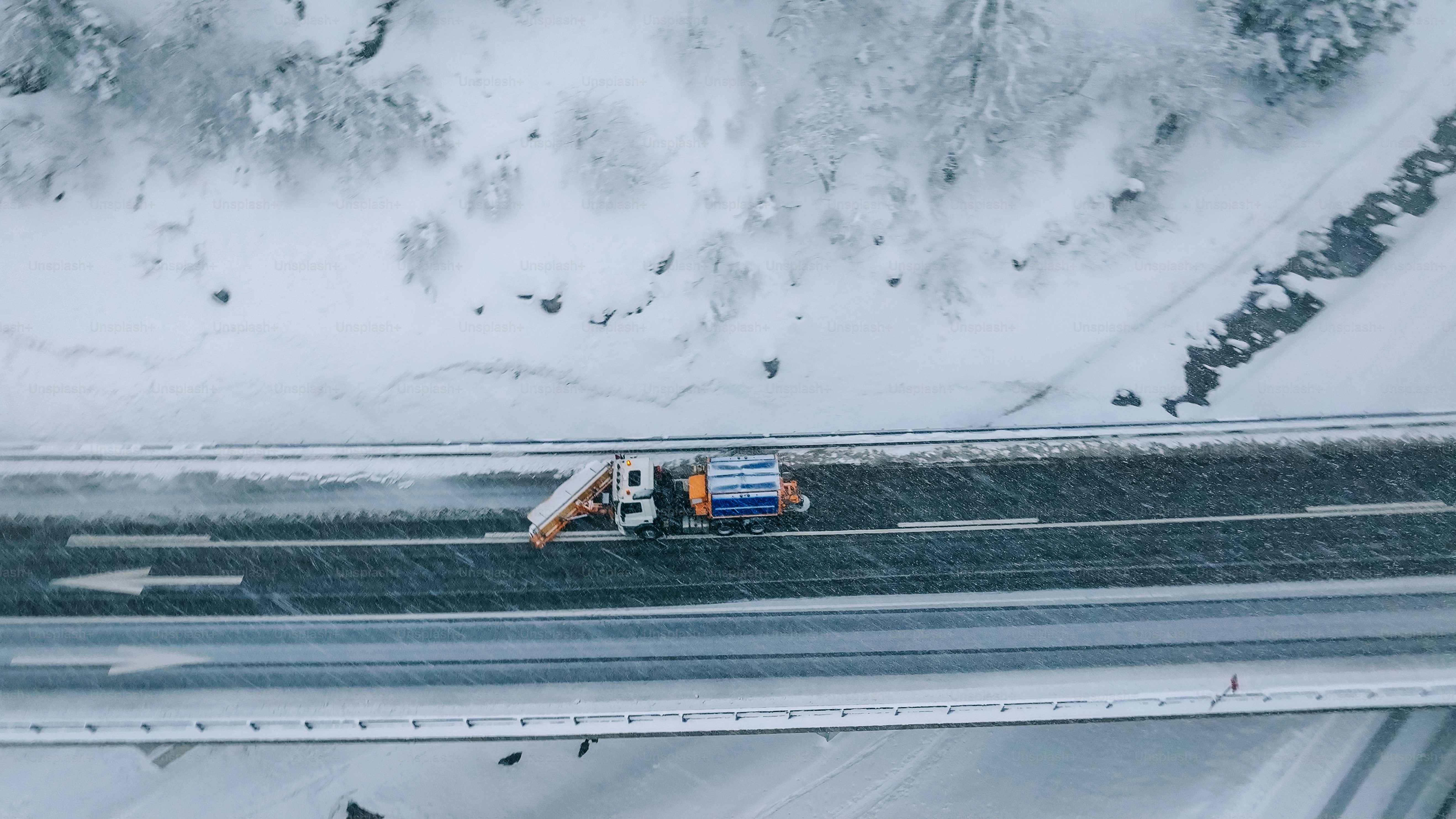 Aerial view of plow truck clearing road on mountain highway during snowstorm