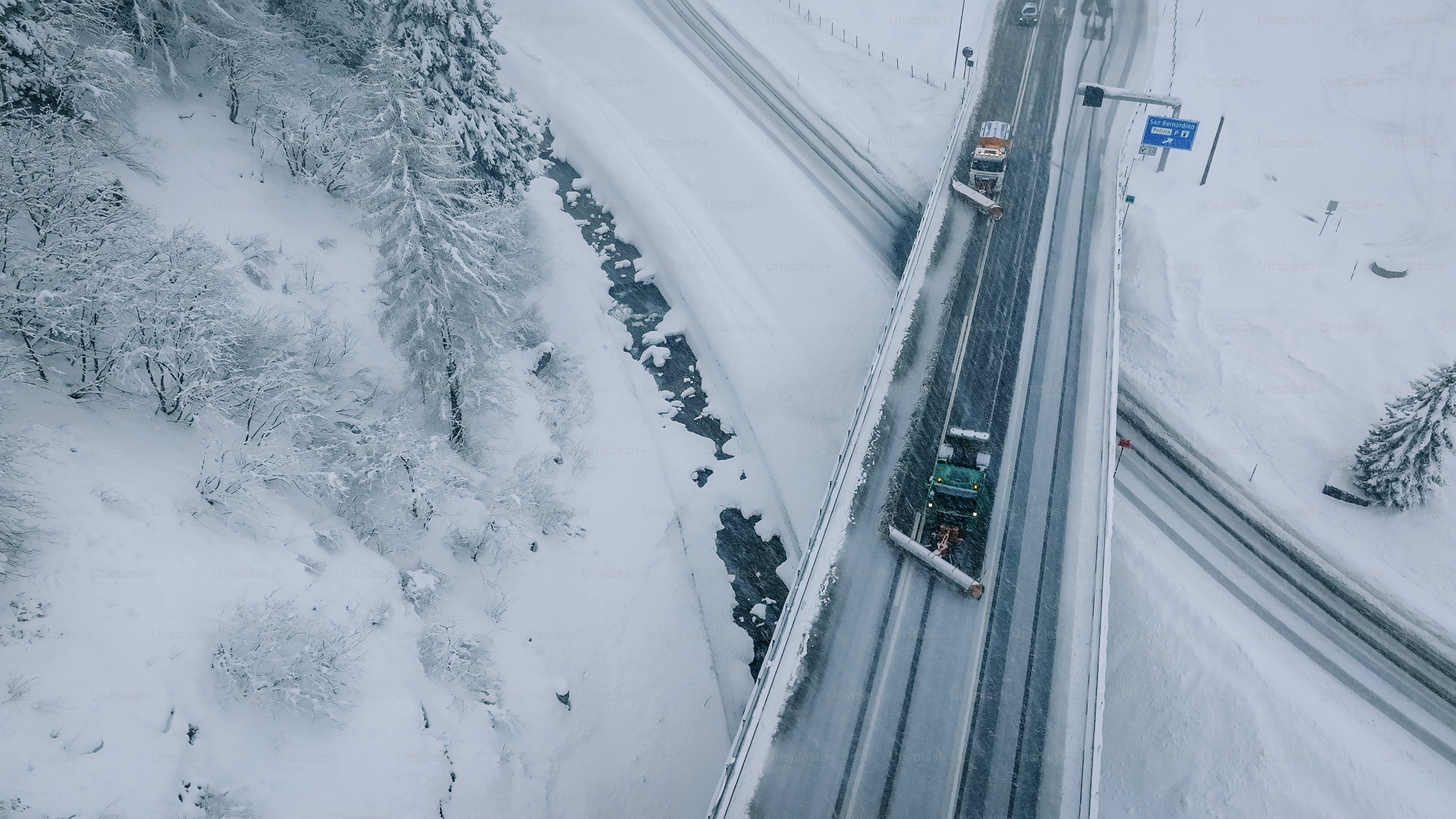 Aerial view of plow truck clearing road on mountain highway during snowstorm
