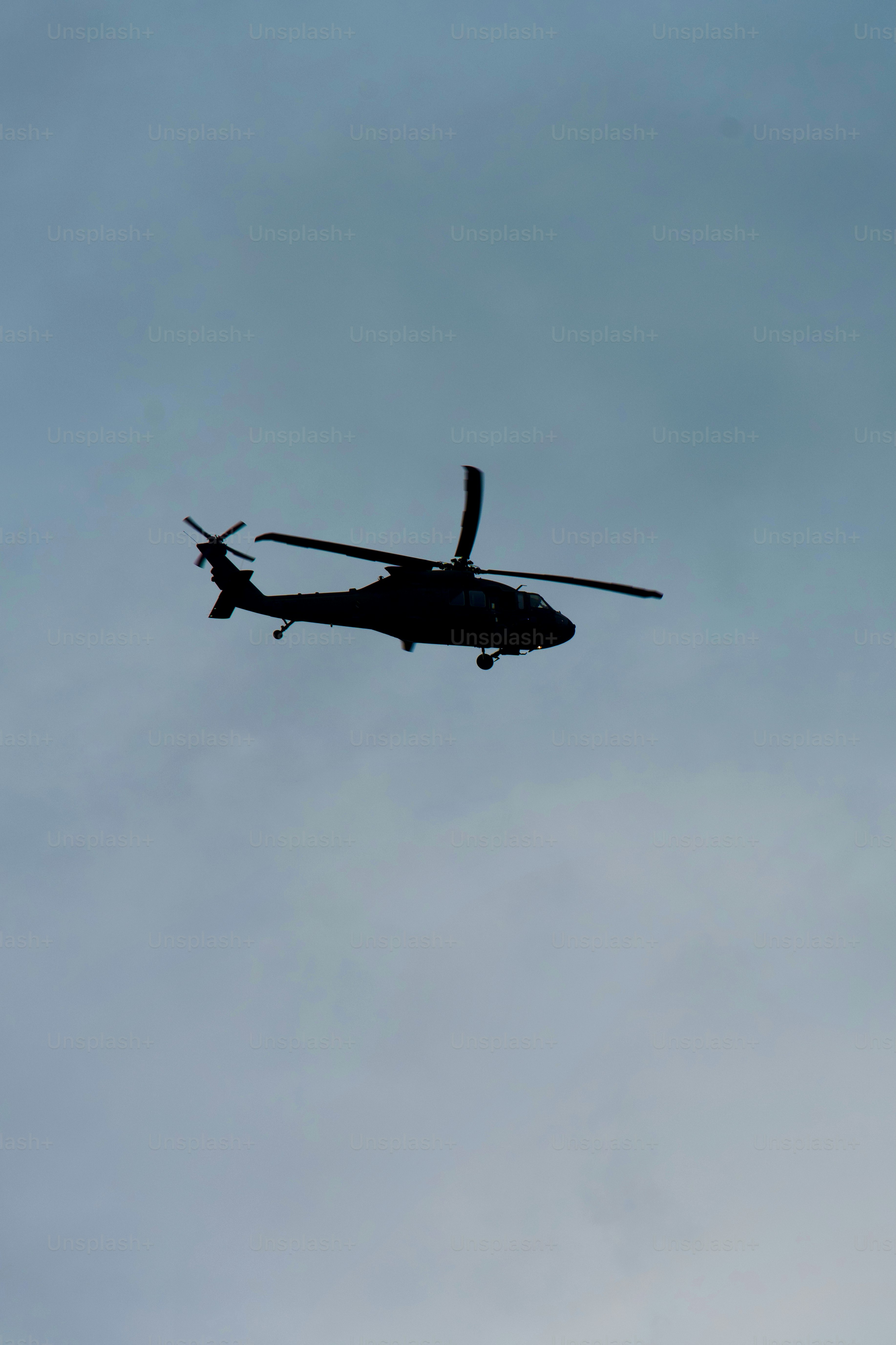 An Army helicopter flies at a low altitude on a cloudy afternoon.