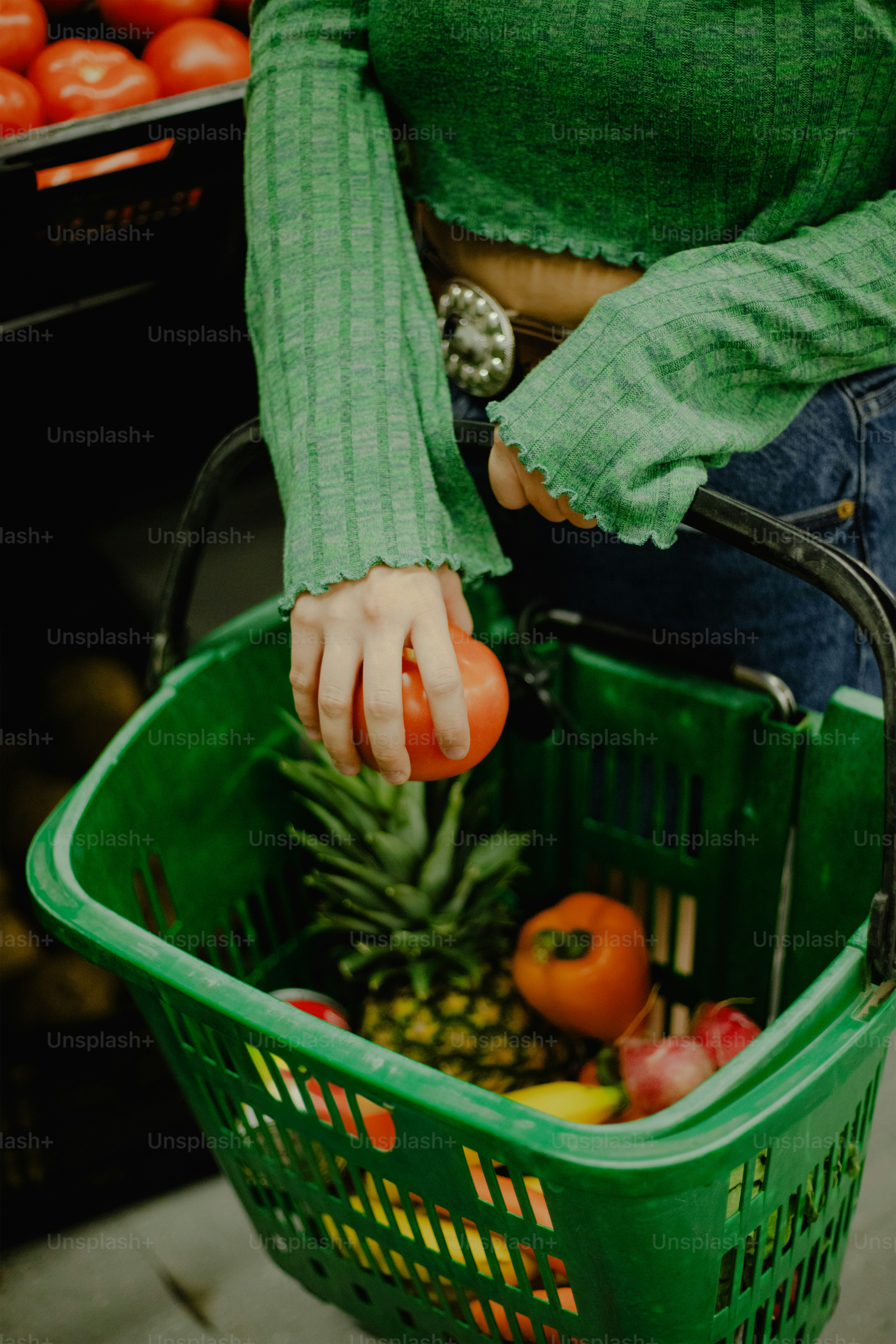 A person places a tomato in a grocery basket.