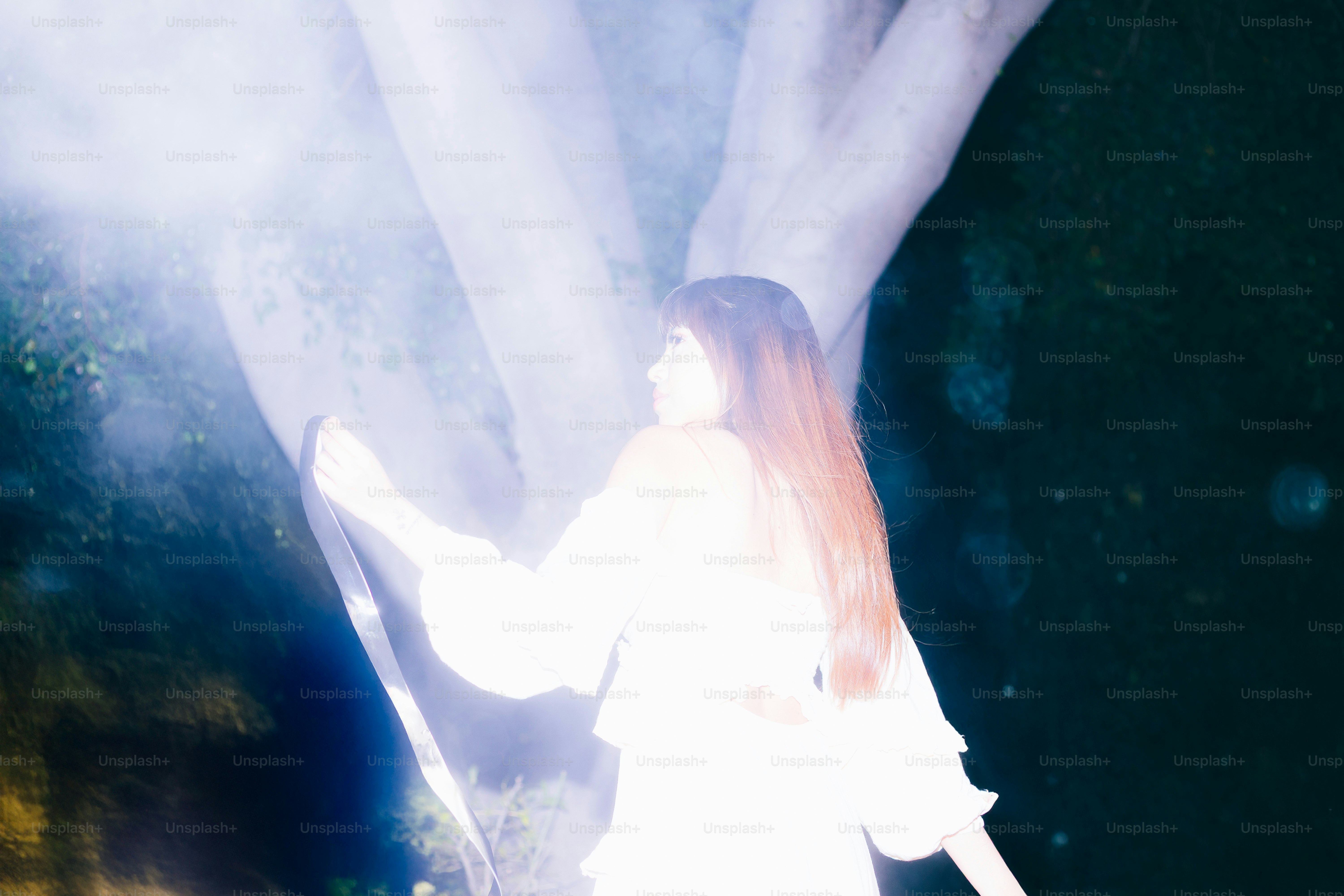 Woman in white stands near a bright light.