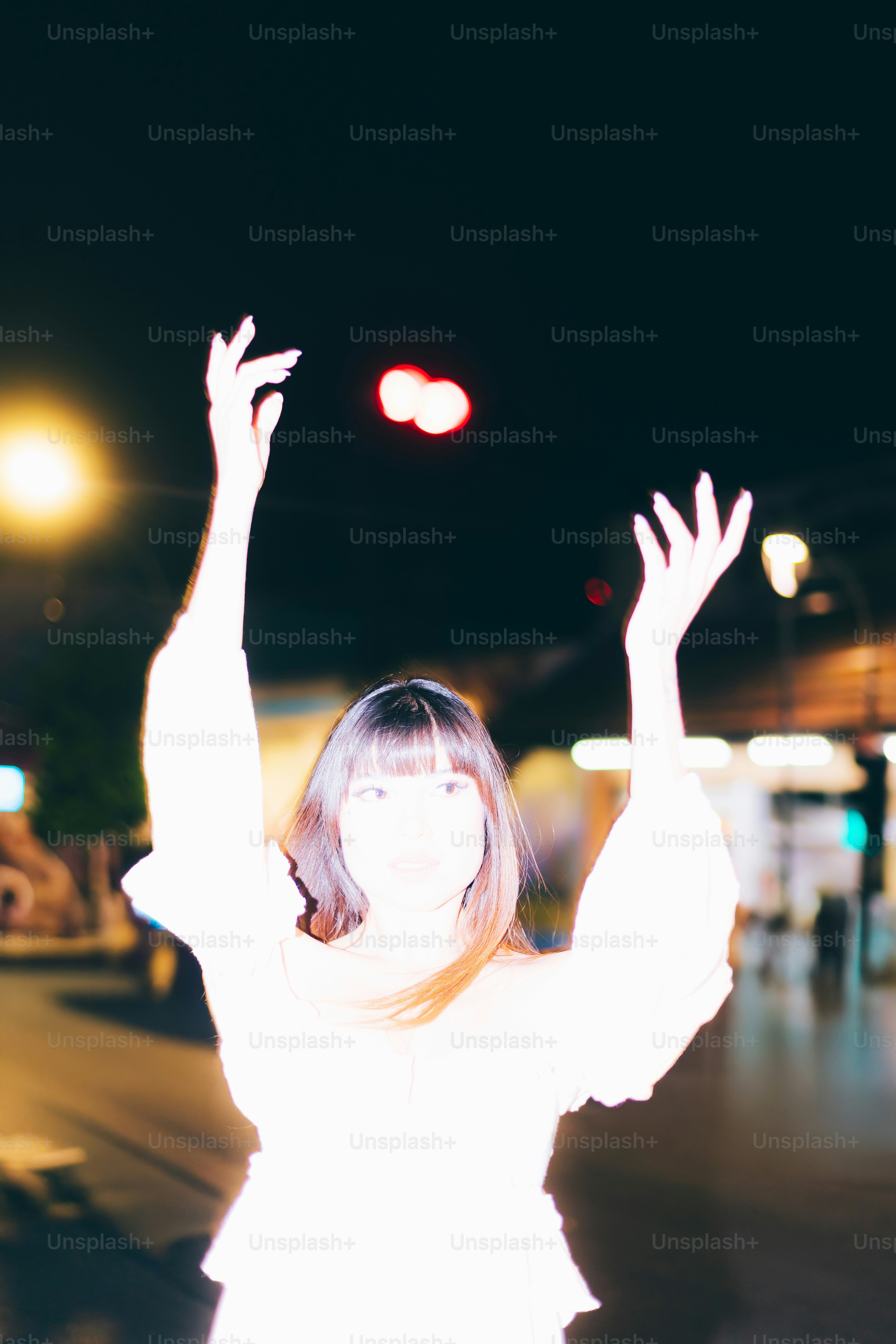 Frau greift nachts mit verschwommenen Lichtern nach oben.