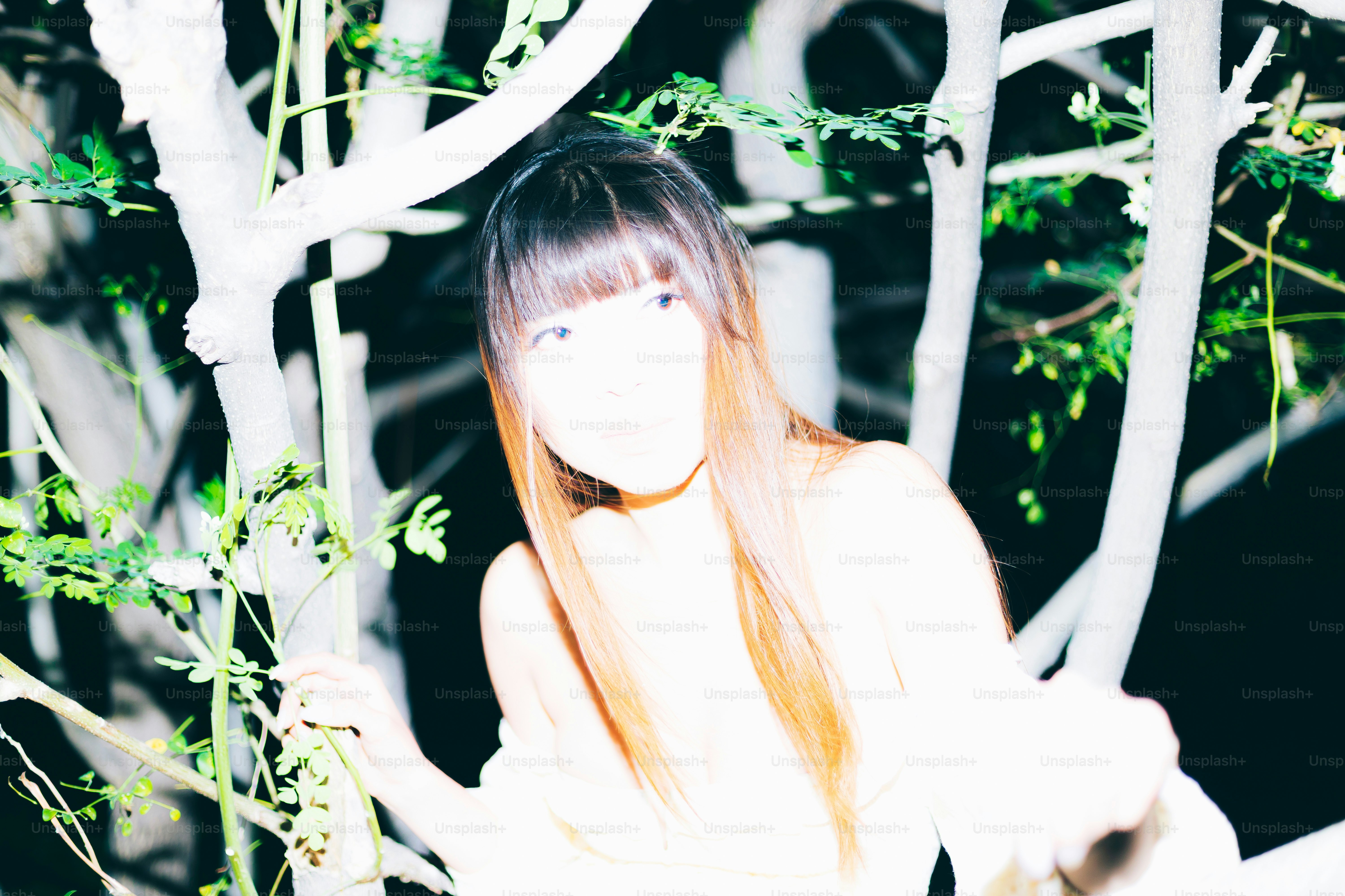 Woman stands amidst branches and foliage.