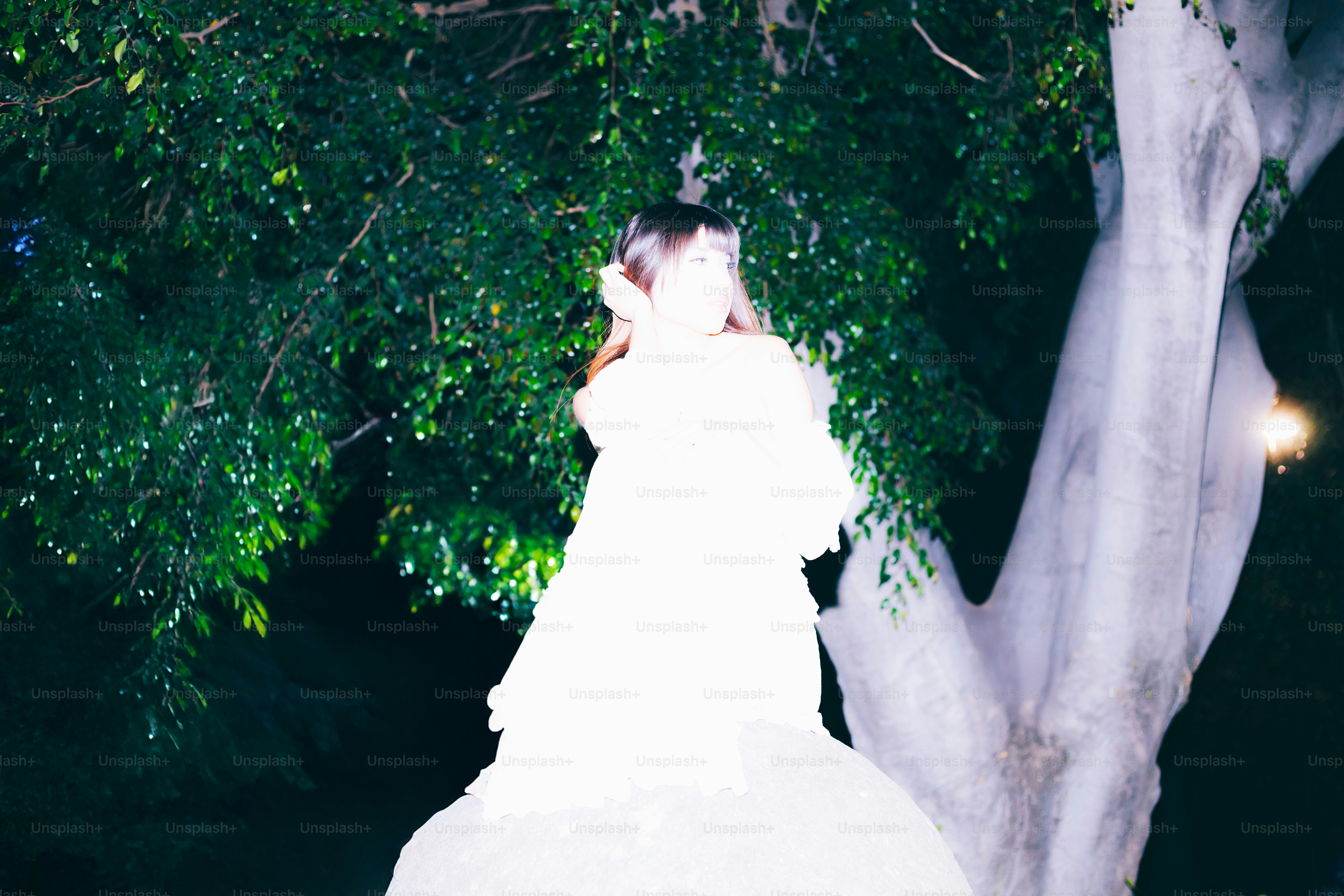 Woman in white stands near a tree at night.