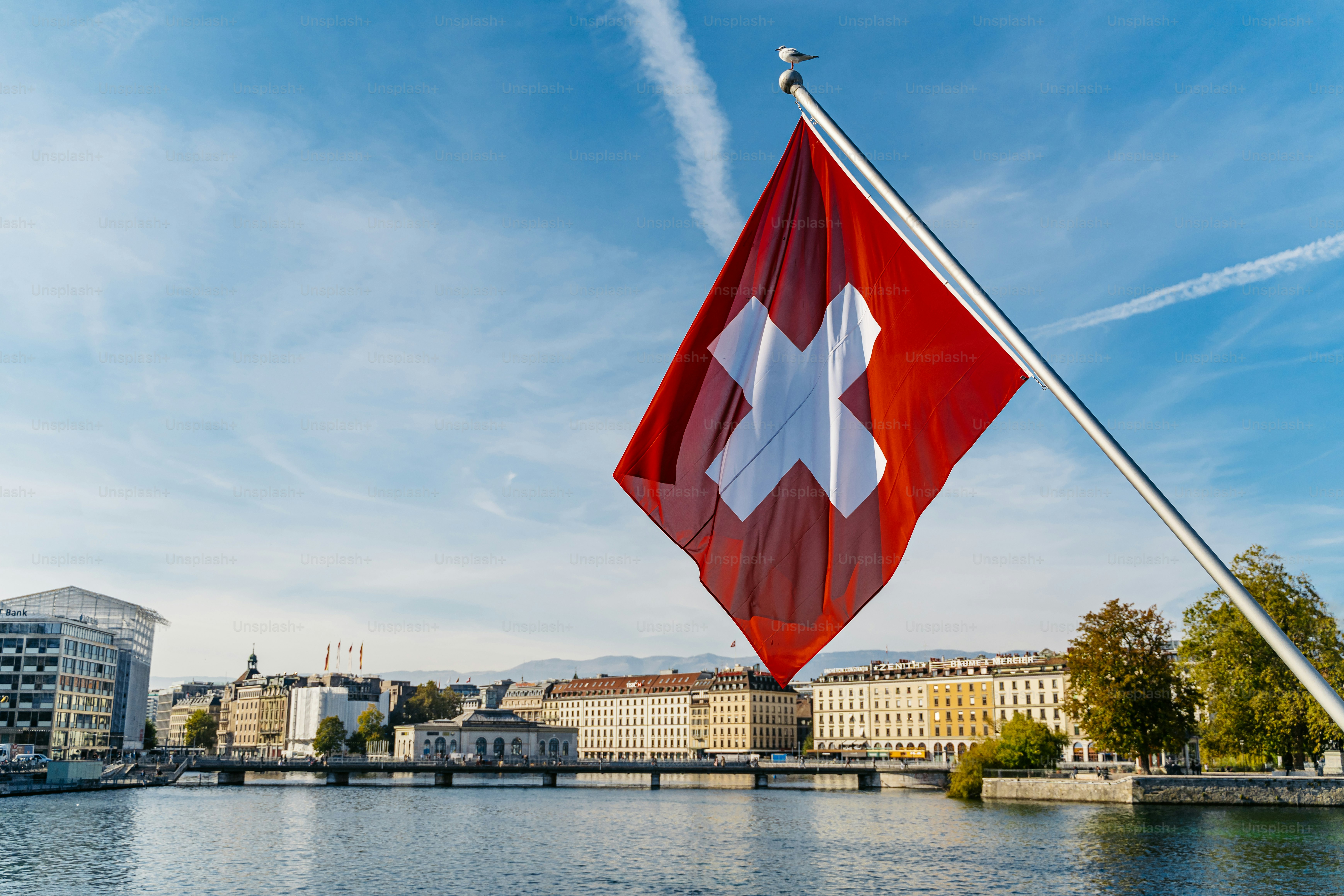 Bandera de Suiza sobre el lago de Ginebra con la ciudad al fondo.