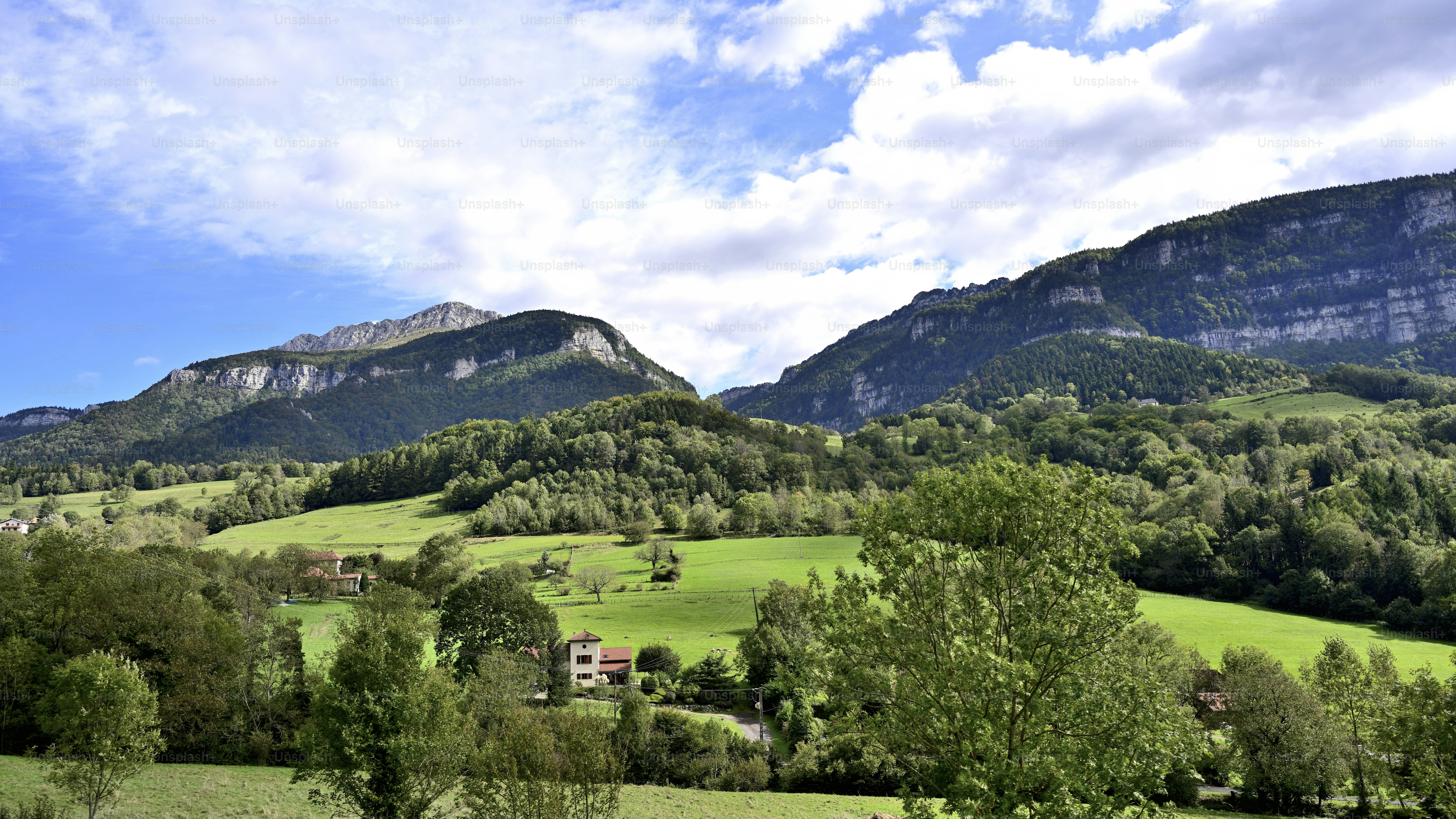 A green valley with a small house below steep rocky mountain slopes