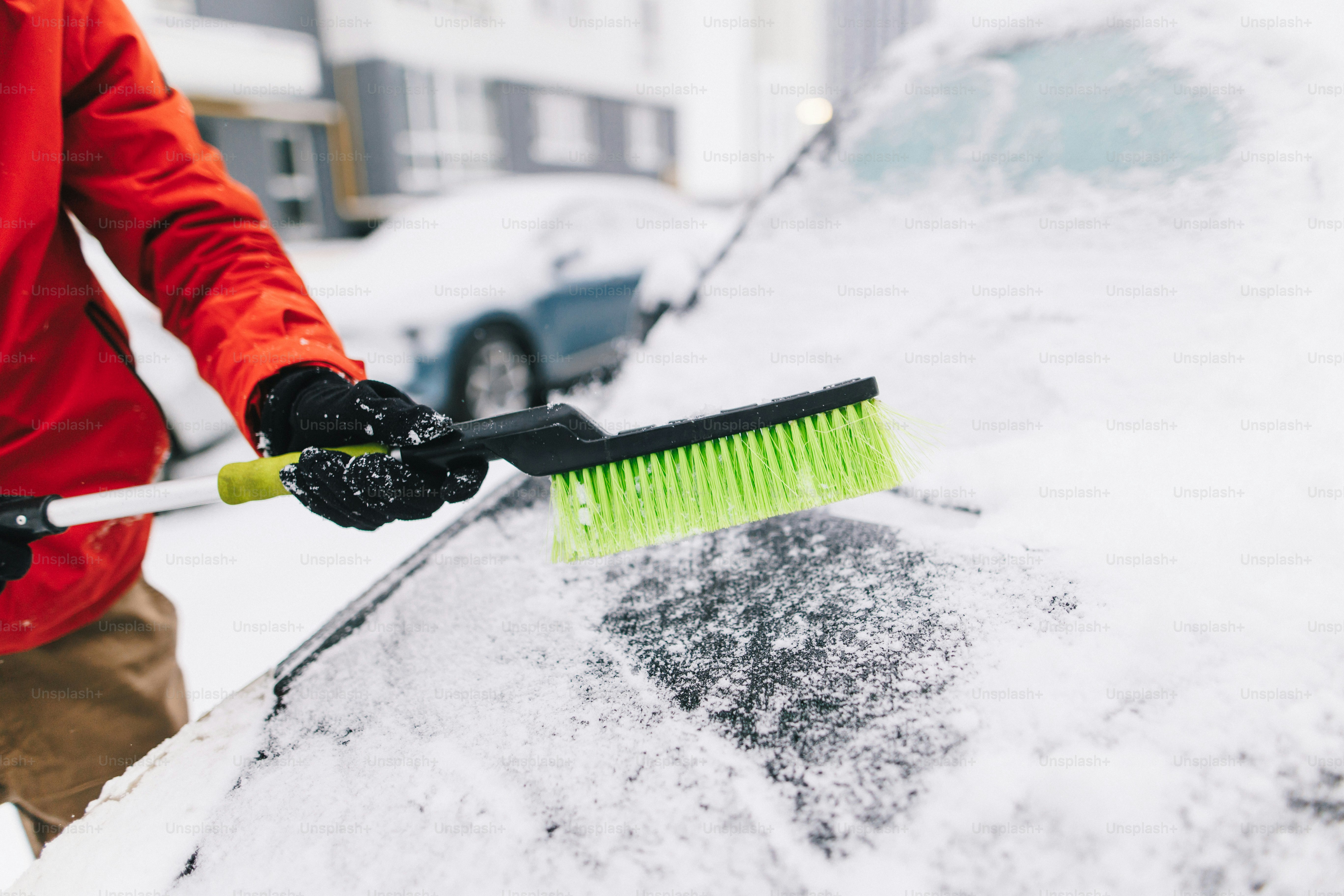 The unrecognisable man cleaning the snow from a car using the profession brush tool, close up view