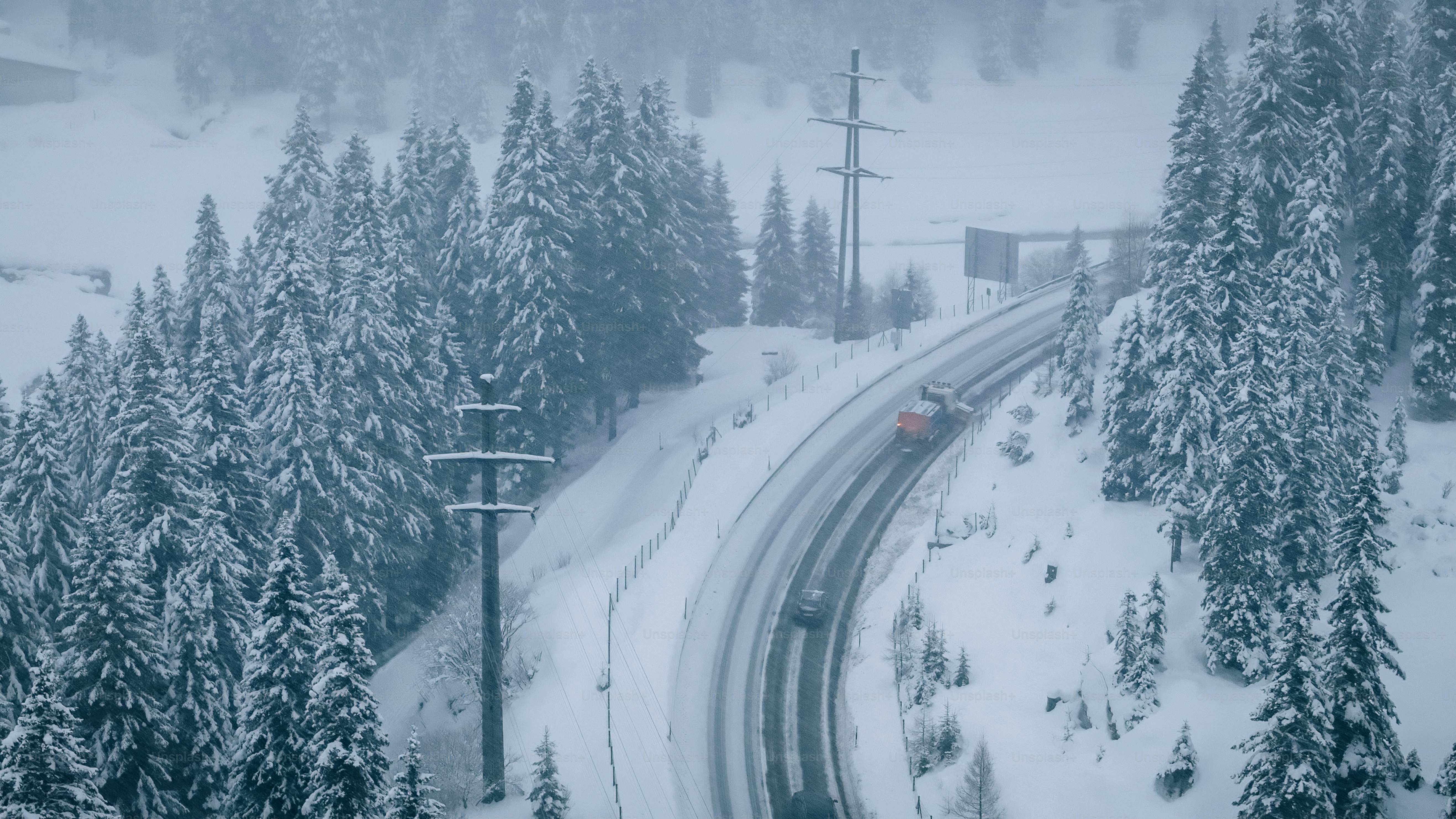 Aerial view of plow truck clearing road on mountain highway during snowstorm