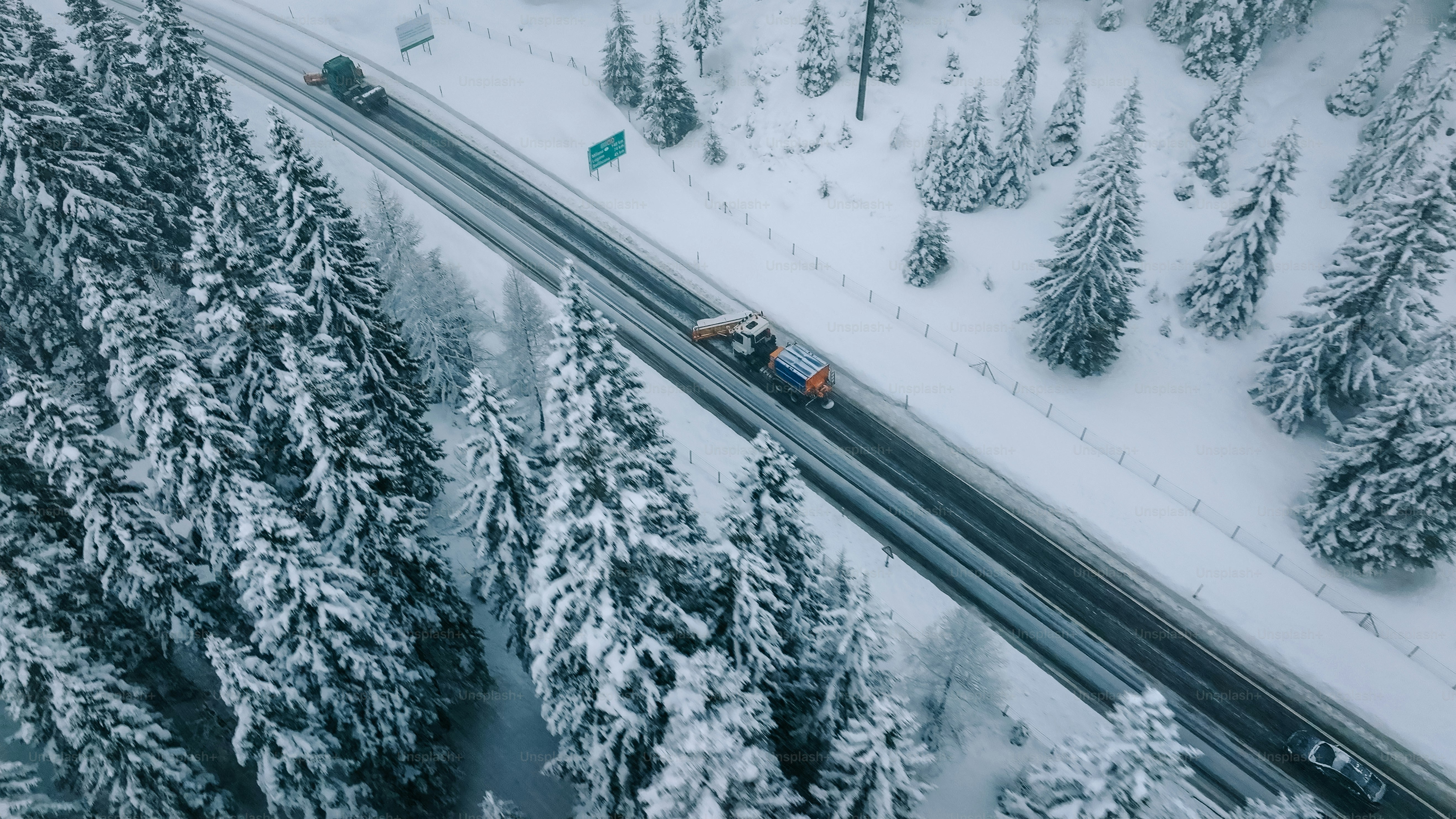 Aerial view of plow truck clearing road on mountain highway during snowstorm
