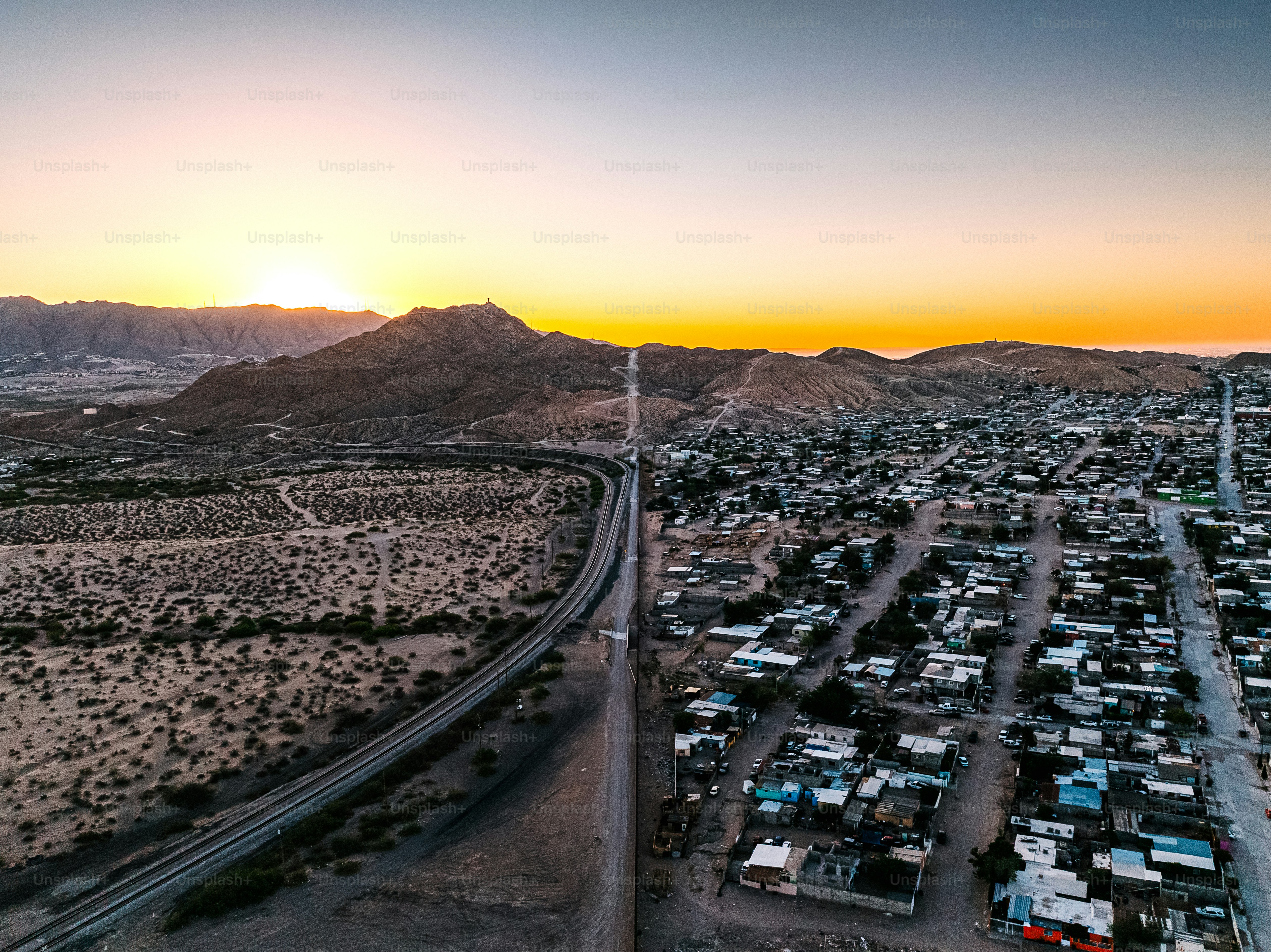 Aerial View of the U.S. Southern Border Wall Fence, (“El Muro Fronterizo,”) separating El Paso and Ciudad Juárez, Mexico in Springtime. The railroad track supports trade between Mexico and the USA. 

Photo taken in the United States.
