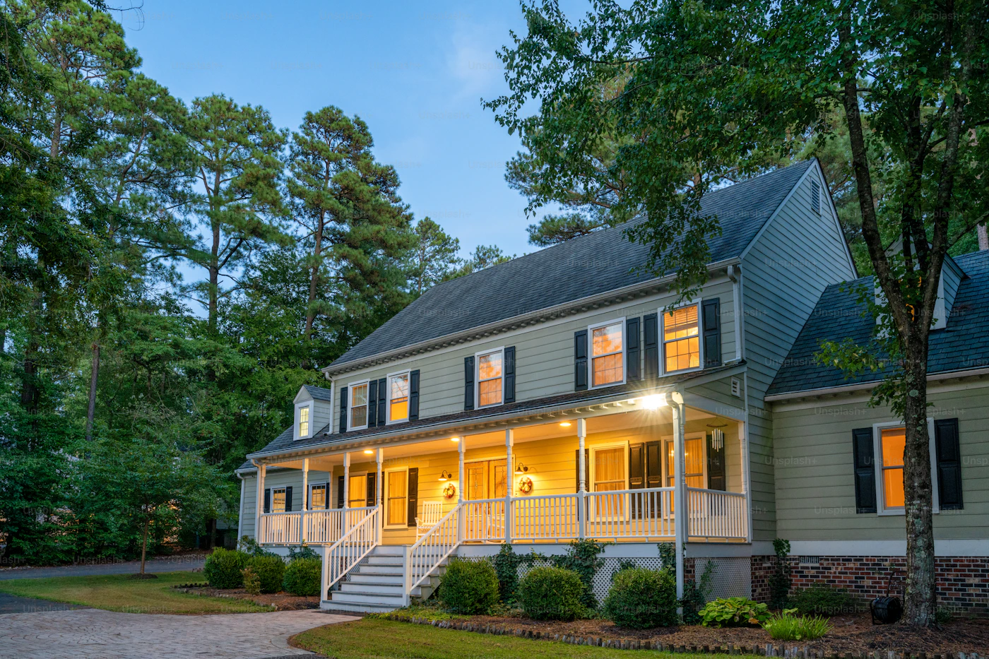 Cream-colored colonial home at dusk with porch lights — Westport