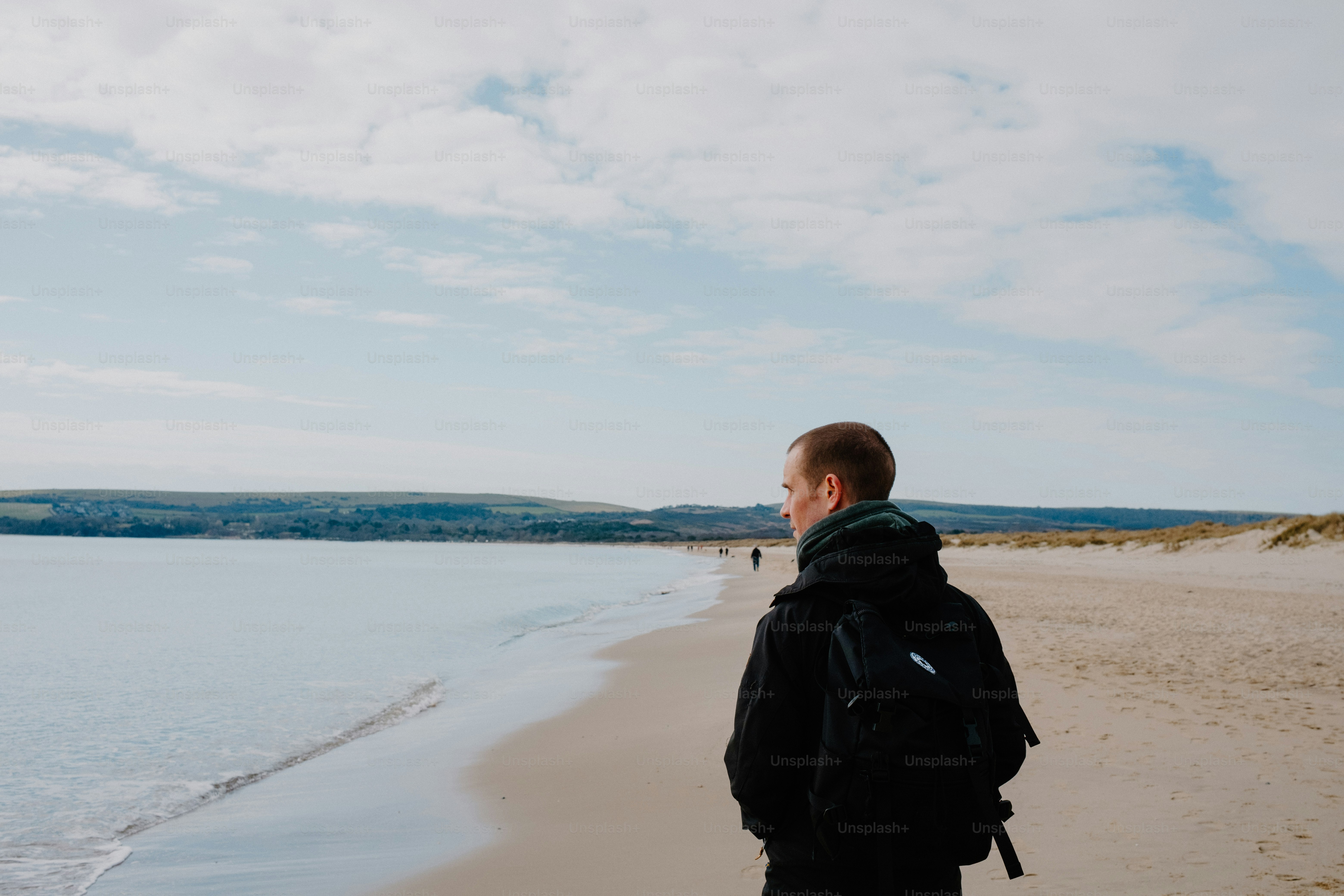 Man with backpack walks alone on a beach.