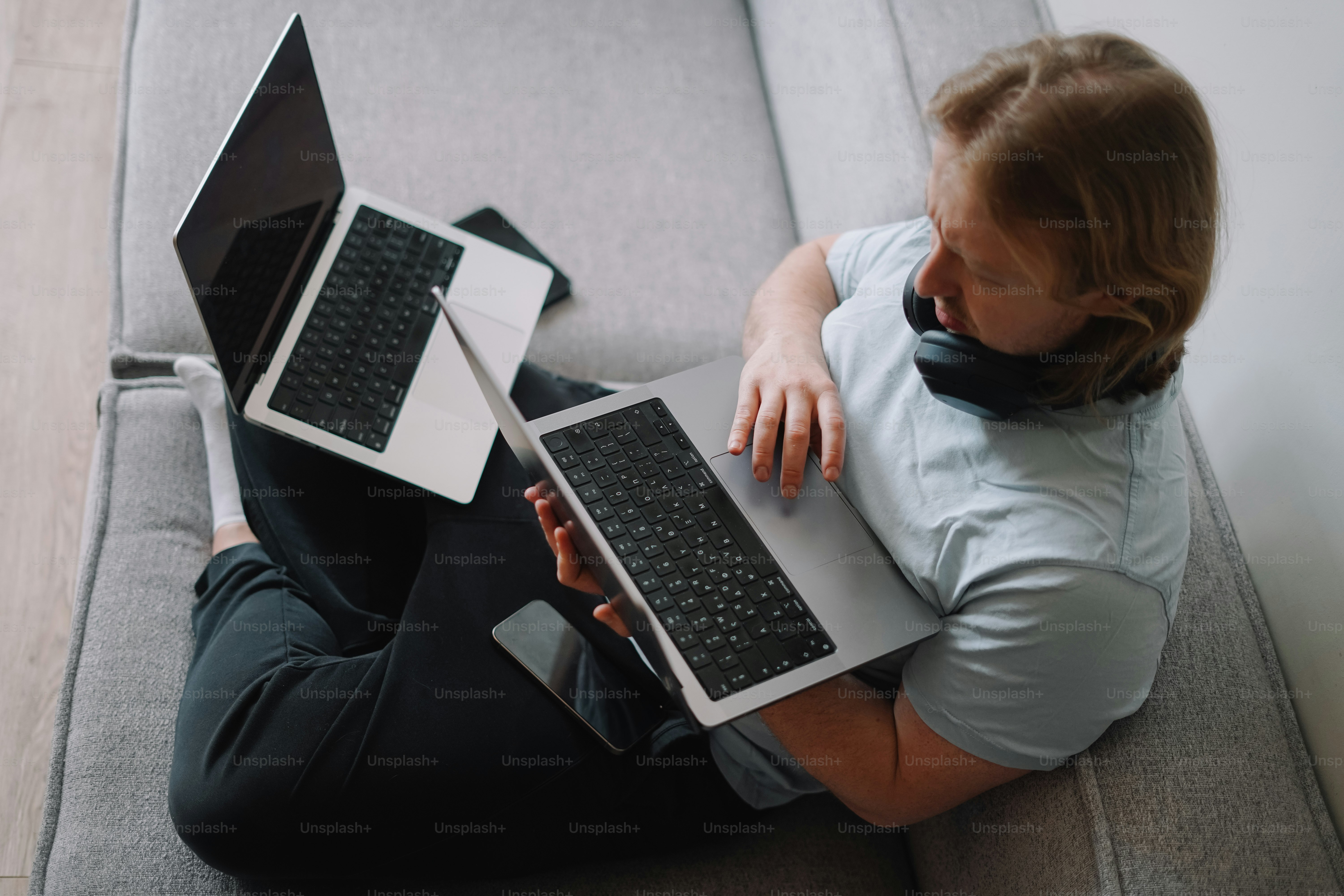 Person uses two laptops while lounging on a couch.