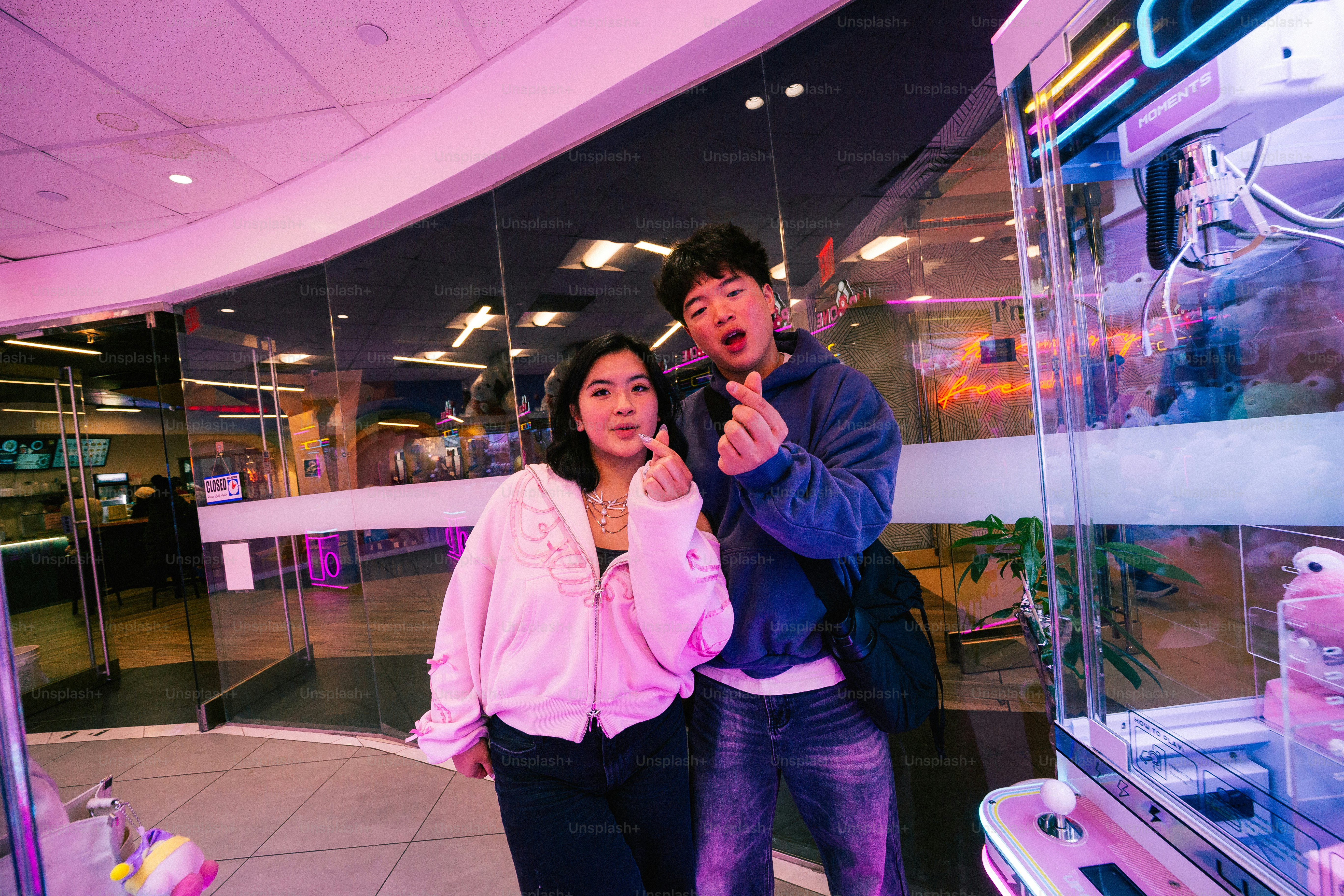 Couple makes a heart gesture near an arcade game.