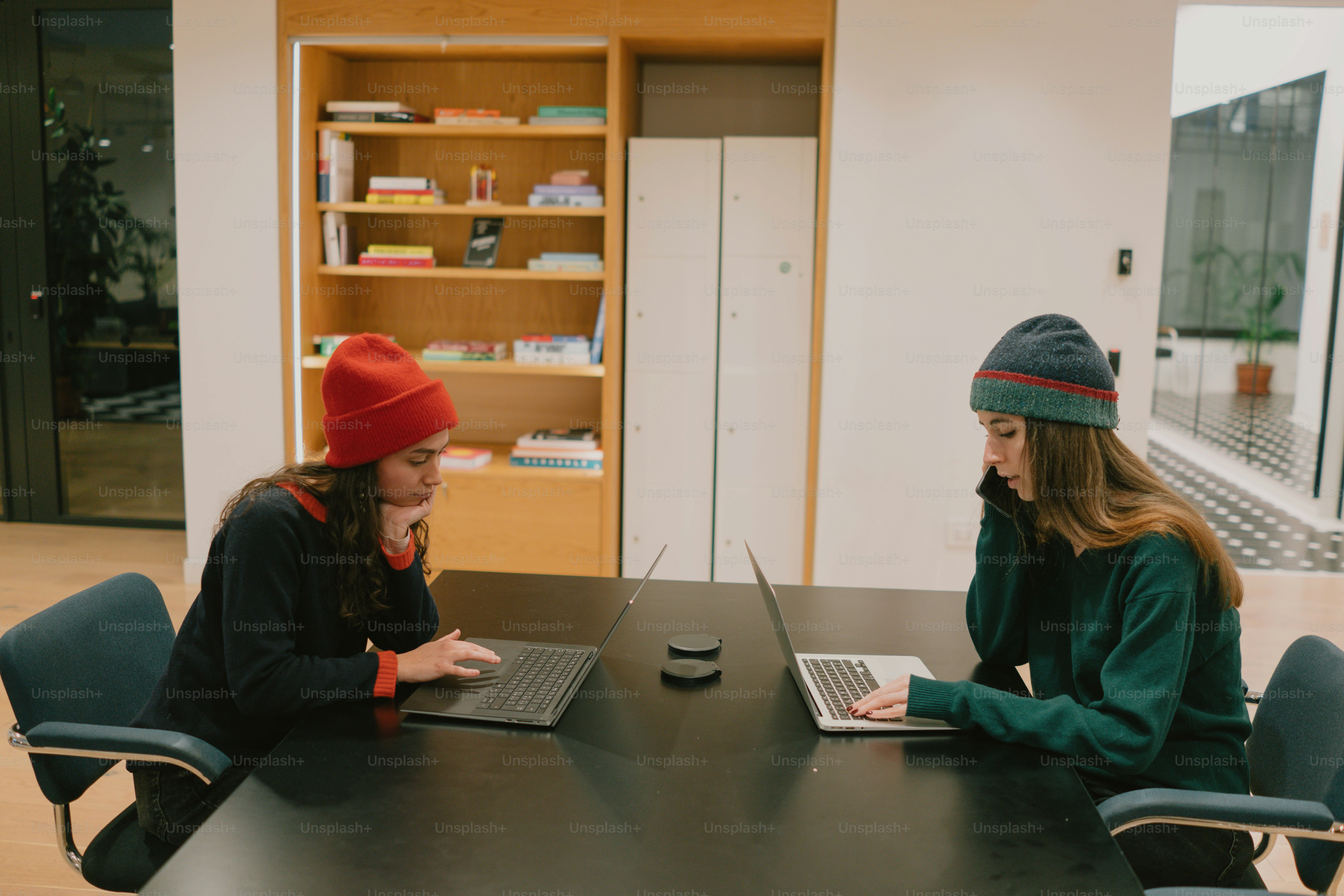 Two women work together at a table on laptops.