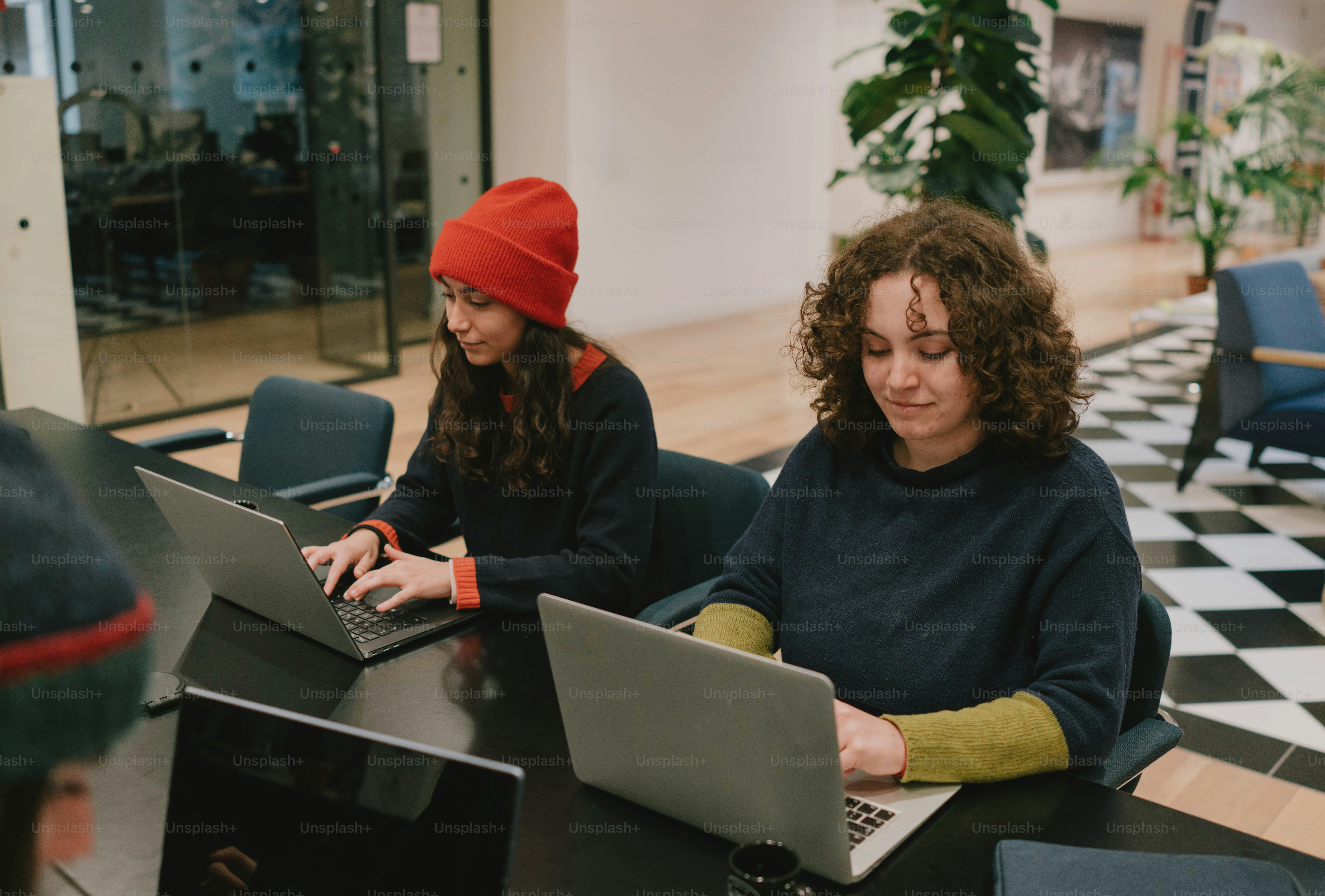 Two women are working on laptops at a table.