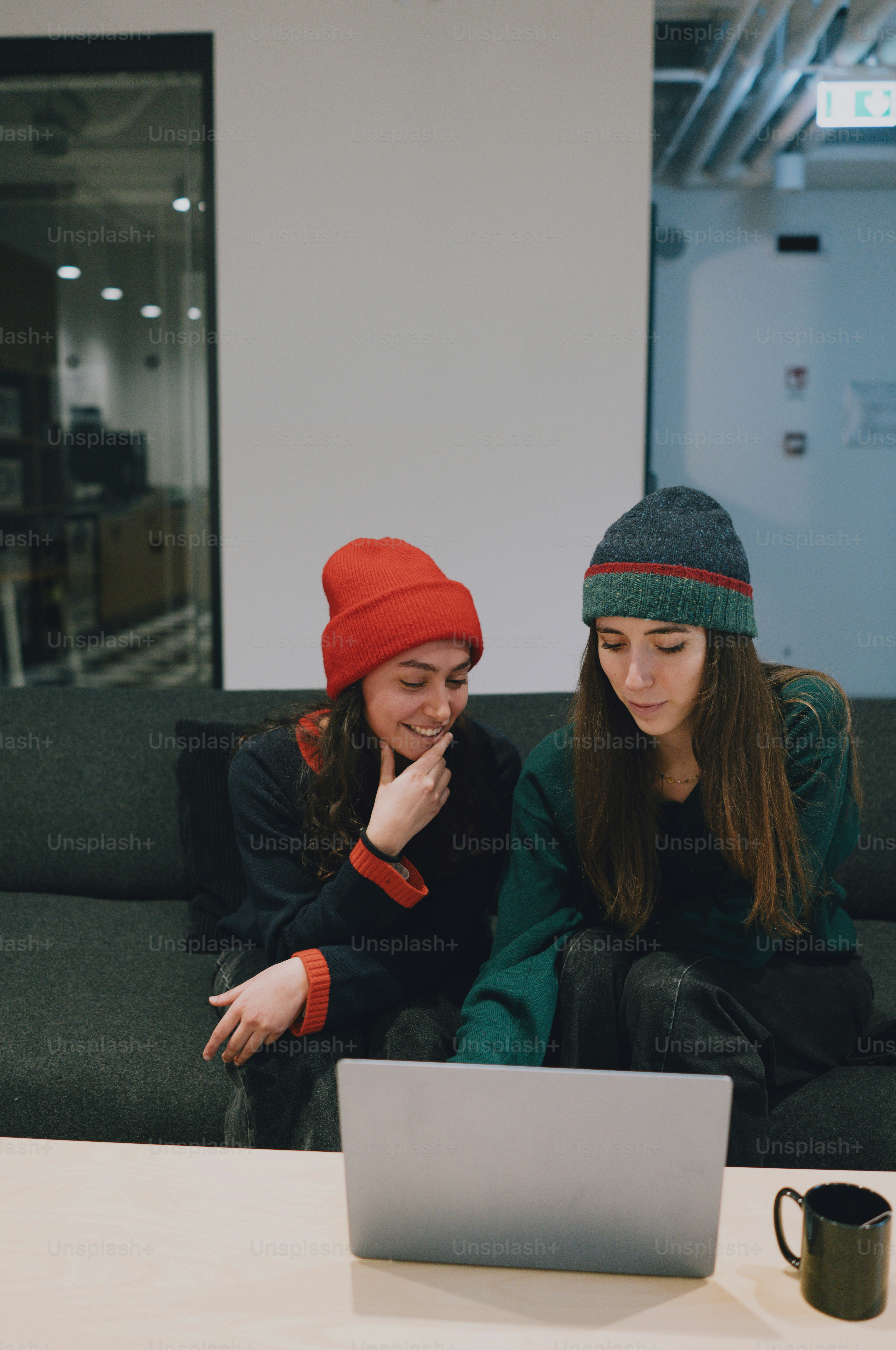 Two women wearing beanies look at a laptop.