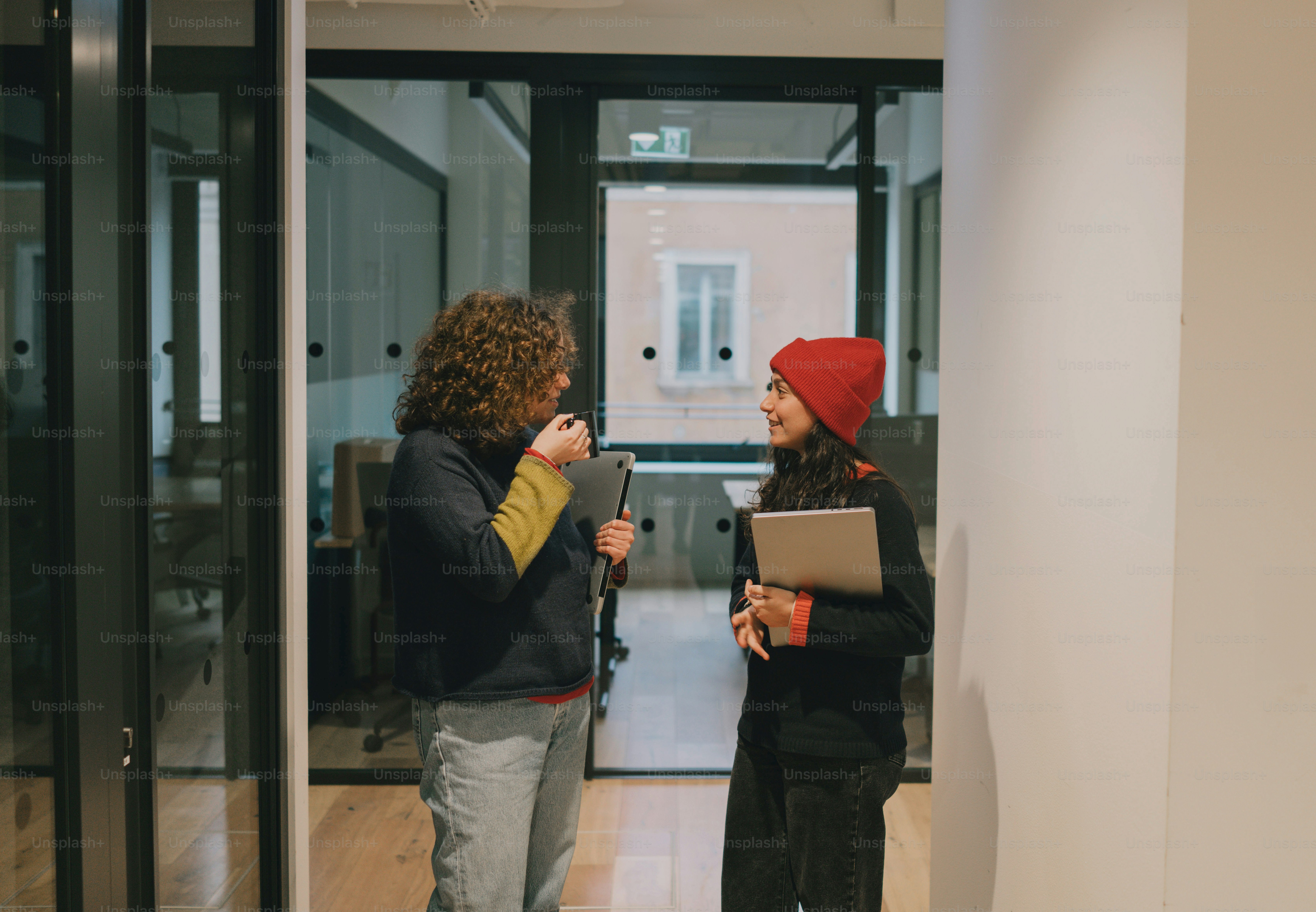 Two women chat in a modern office setting.
